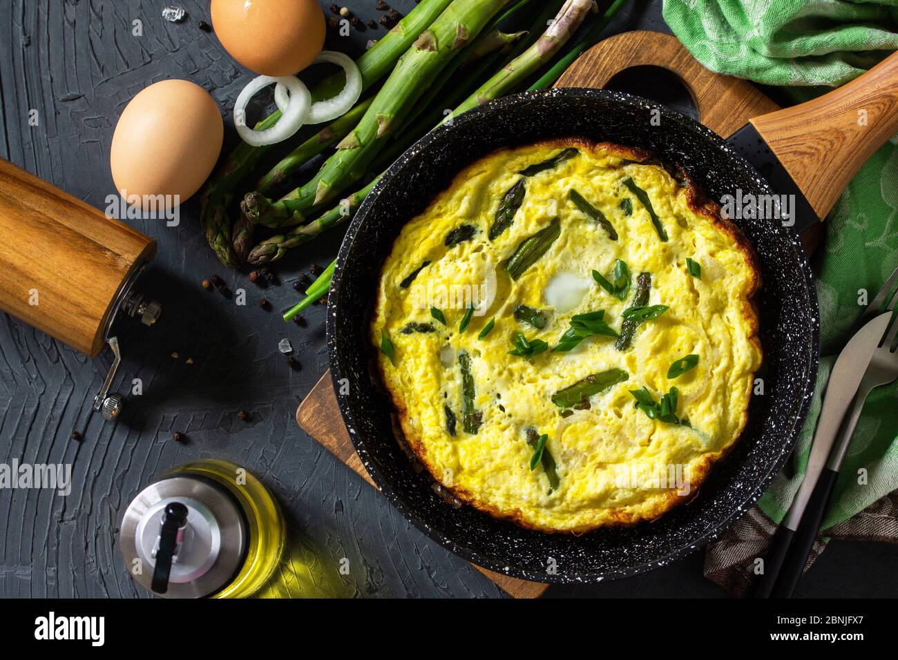 Omelette aux asperges saines. Omelette aux oeufs avec asperges et oignons dans une poêle en fonte sur un comptoir en pierre. Vue de dessus de l'arrière-plan de la mise à plat Banque D'Images