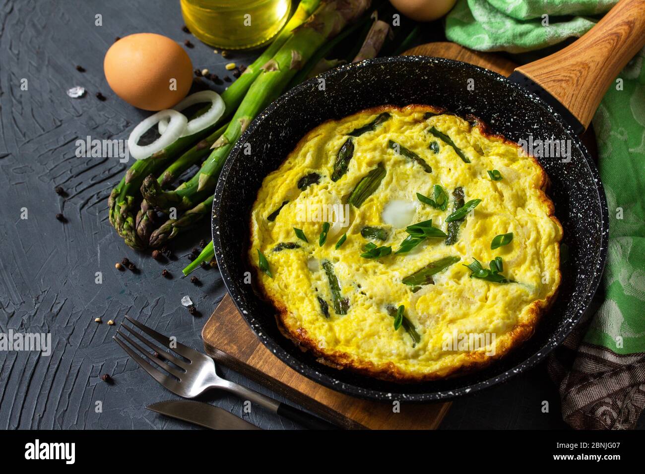 Omelette aux asperges saines. Omelette aux oeufs avec asperges et oignons dans une poêle en fonte sur un comptoir en pierre. Copier l'espace. Banque D'Images