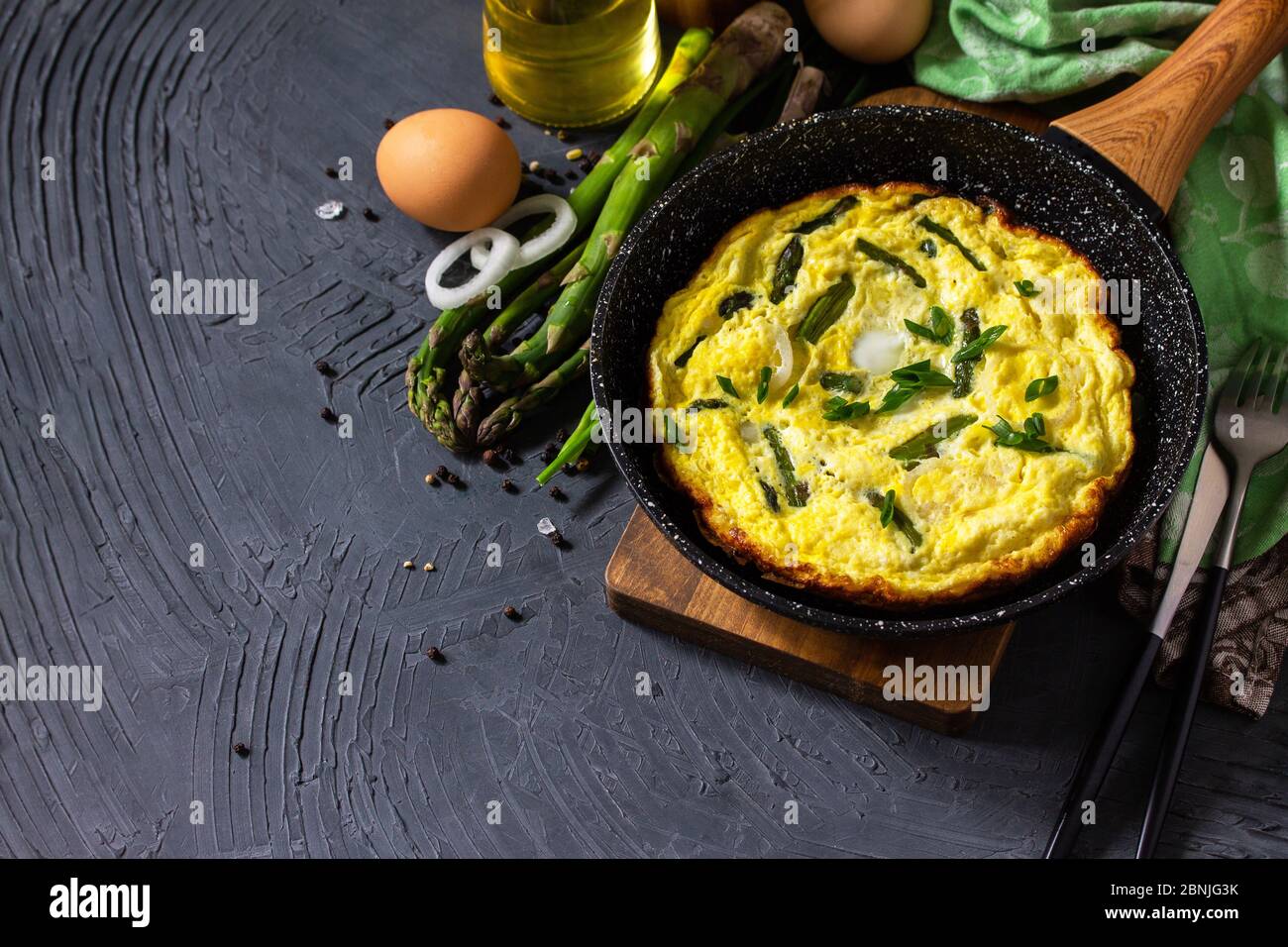 Omelette aux asperges saines. Omelette aux oeufs avec asperges et oignons dans une poêle en fonte sur un comptoir en pierre. Copier l'espace. Banque D'Images
