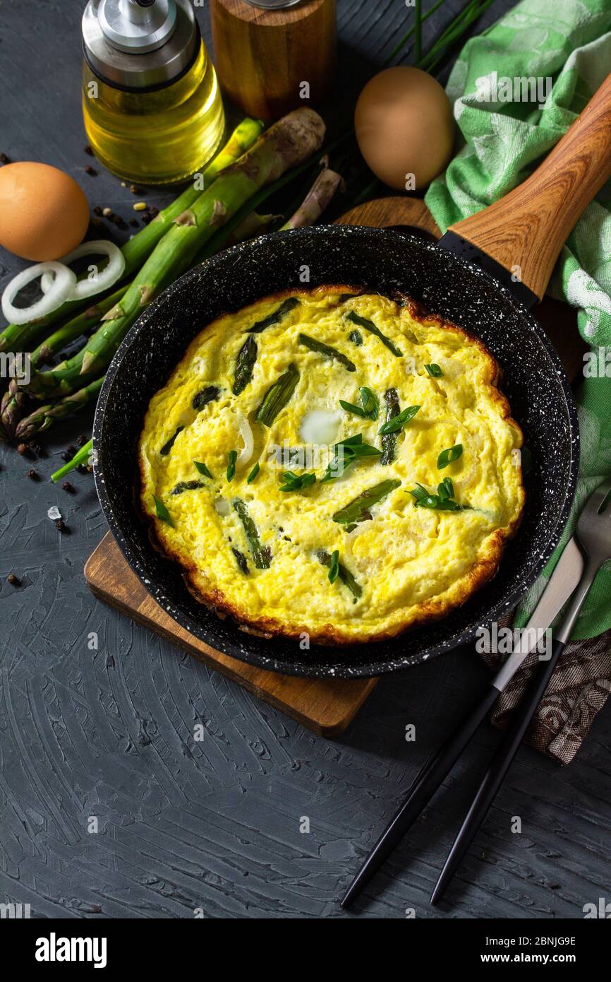 Omelette aux asperges saines. Omelette aux oeufs avec asperges et oignons dans une poêle en fonte sur un comptoir en pierre. Copier l'espace. Banque D'Images