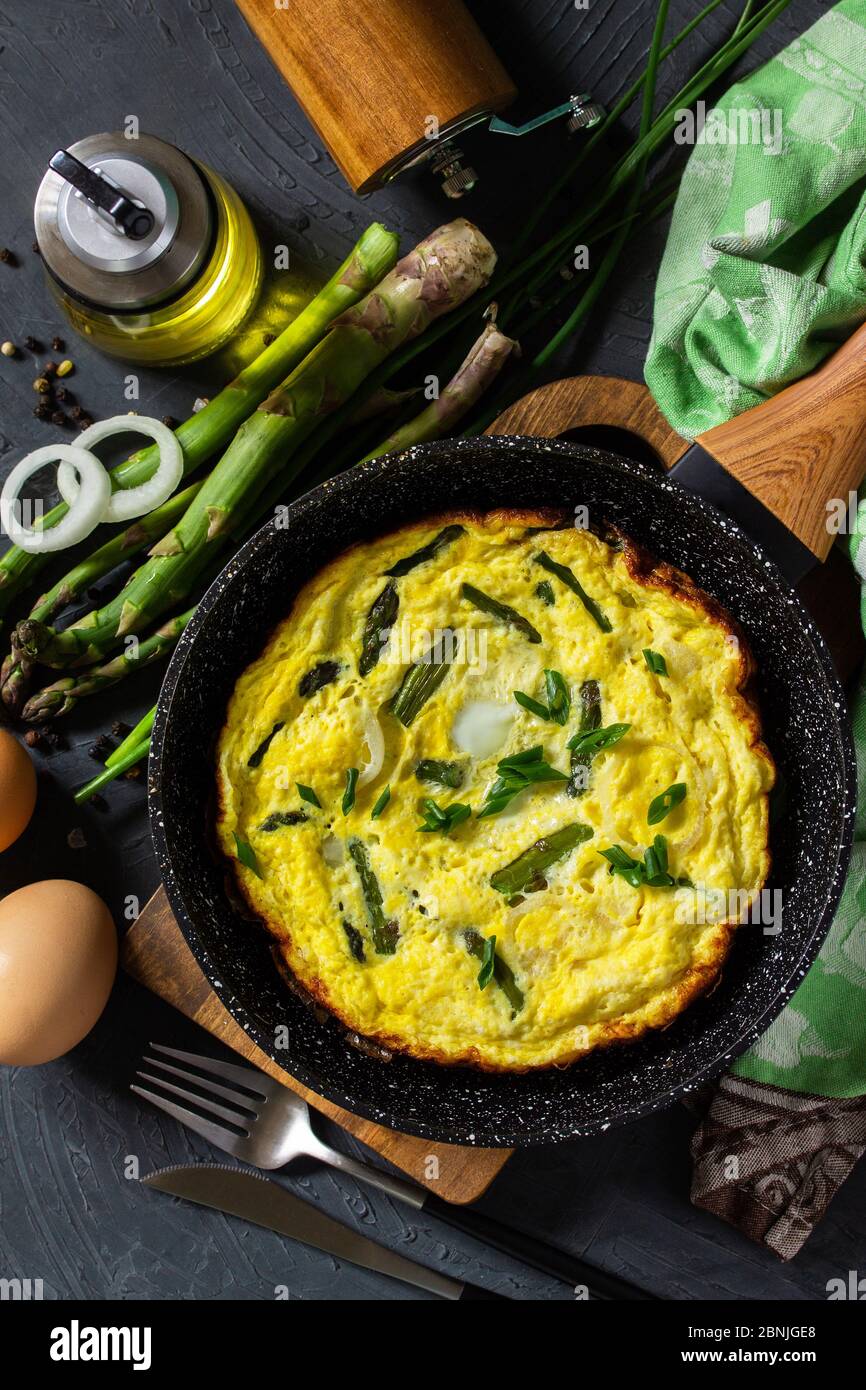 Omelette aux asperges saines. Omelette aux oeufs avec asperges et oignons dans une poêle en fonte sur un comptoir en pierre. Vue de dessus de l'arrière-plan de la mise à plat Banque D'Images