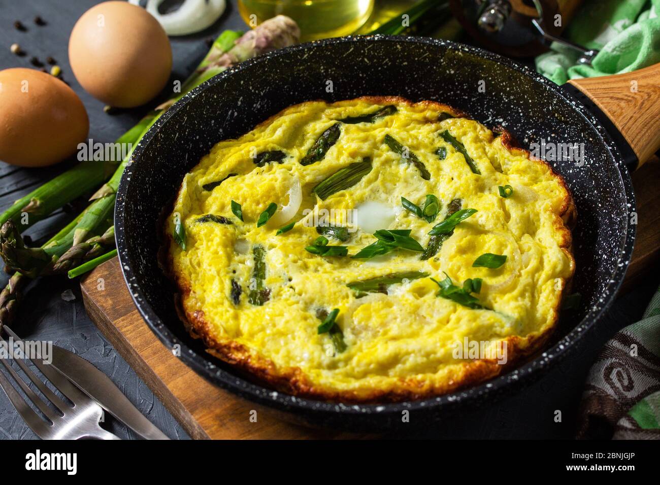 Omelette aux asperges saines. Omelette aux oeufs avec asperges et oignons dans une poêle en fonte sur un comptoir en pierre. Banque D'Images