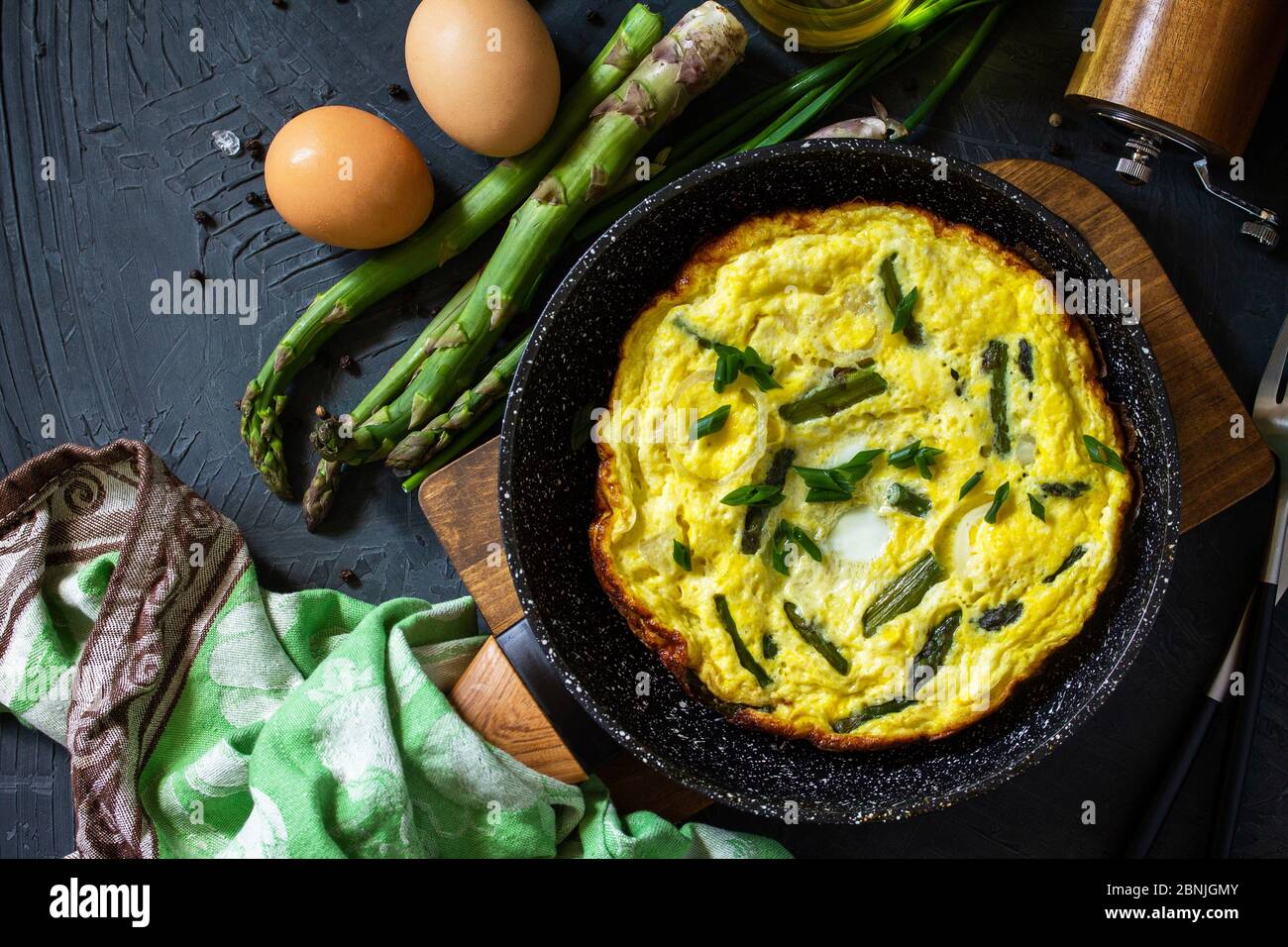 Omelette aux asperges saines. Omelette aux oeufs avec asperges et oignons dans une poêle en fonte sur un comptoir en pierre. Vue de dessus de l'arrière-plan de la mise à plat Banque D'Images