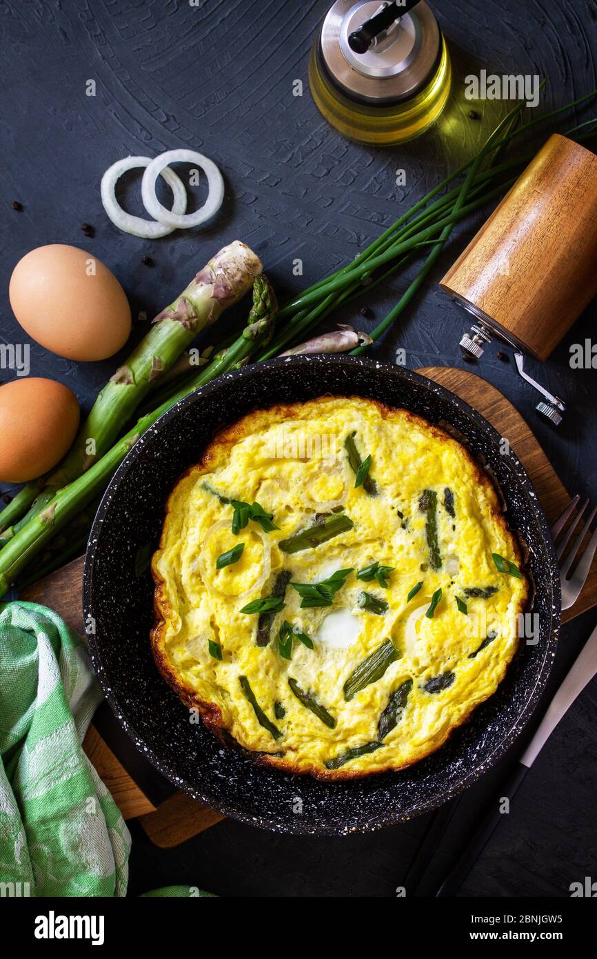 Omelette aux asperges saines. Omelette aux oeufs avec asperges et oignons dans une poêle en fonte sur un comptoir en pierre. Vue de dessus de l'arrière-plan de la mise à plat Banque D'Images
