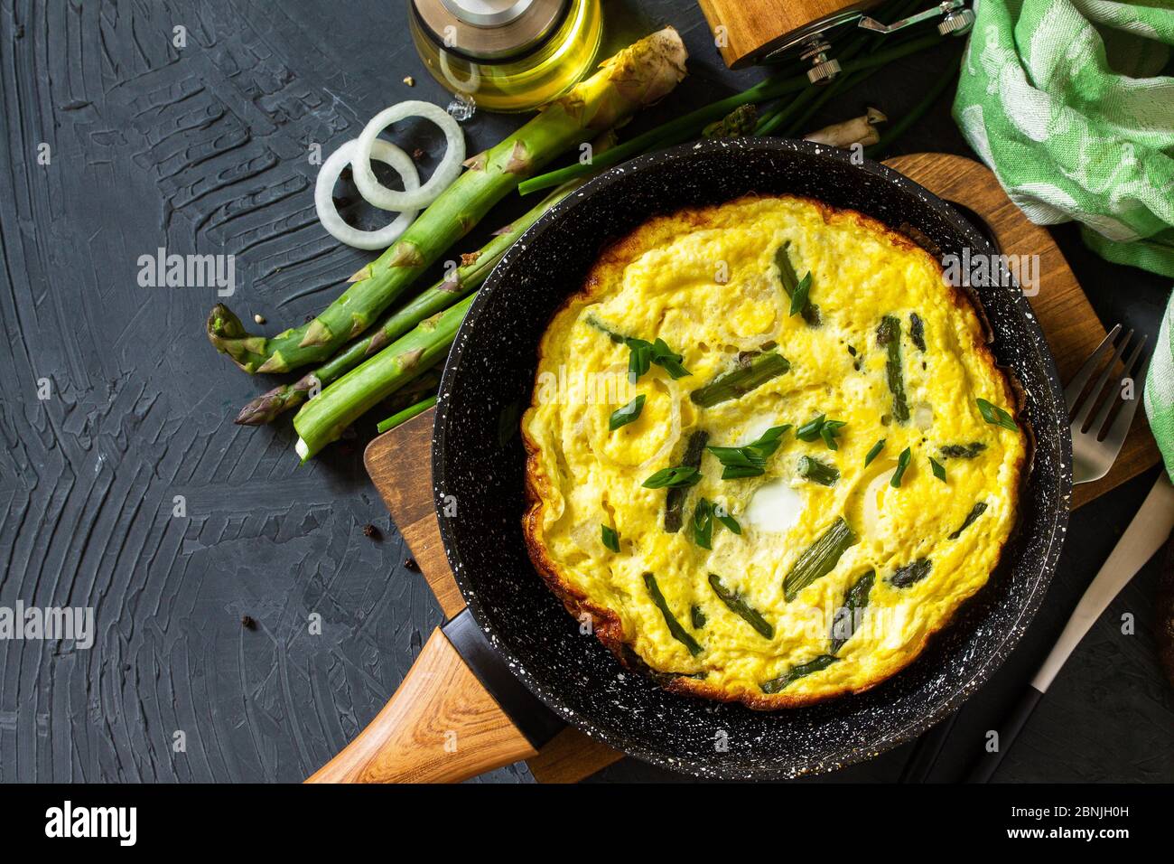 Omelette aux asperges saines. Omelette aux oeufs avec asperges et oignons dans une poêle en fonte sur un comptoir en pierre. Vue de dessus de l'arrière-plan de la mise à plat Copier l'espace. Banque D'Images