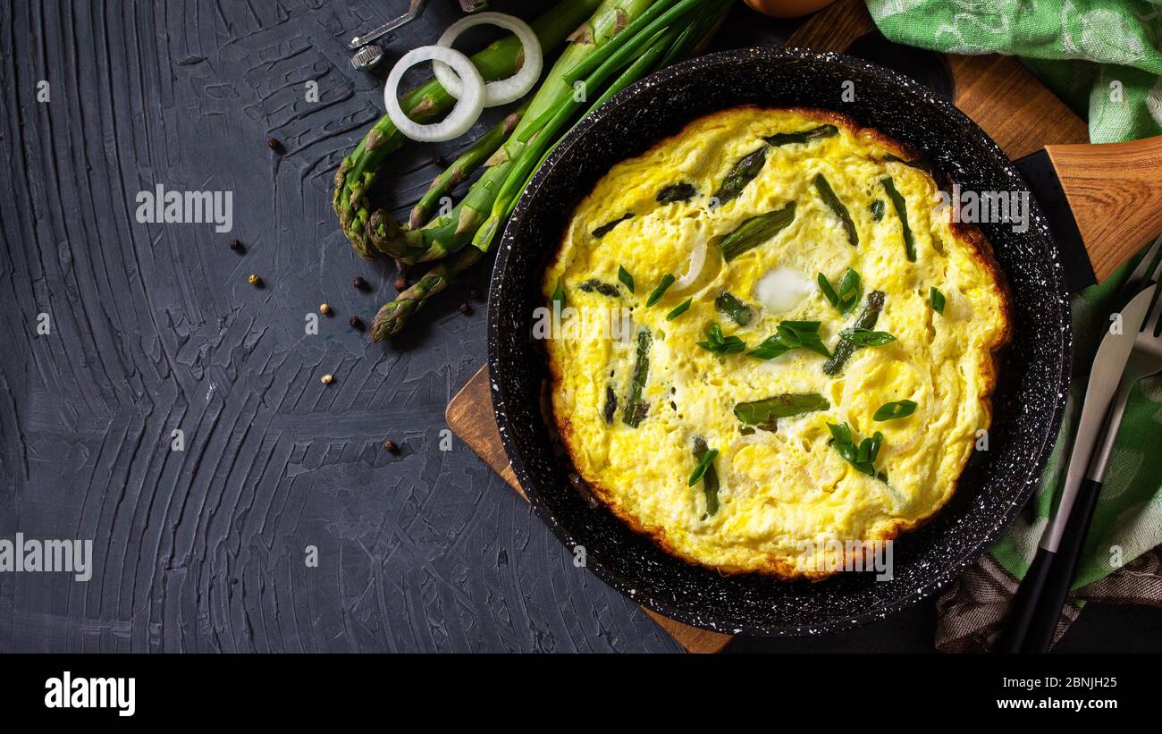 Omelette aux asperges saines. Omelette aux oeufs avec asperges et oignons dans une poêle en fonte sur un comptoir en pierre. Vue de dessus de l'arrière-plan de la mise à plat Bannière. Banque D'Images