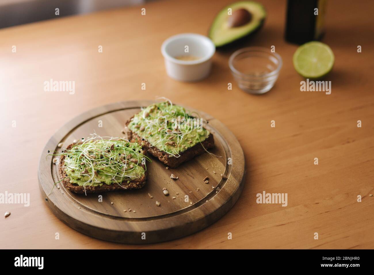 Toast végétalien avec guacamole sur panneau de bois. Pain grillé au seigle avec avocat sur le dessus. Fond des ingrédients. Avocat, lime, huile d'olive Banque D'Images