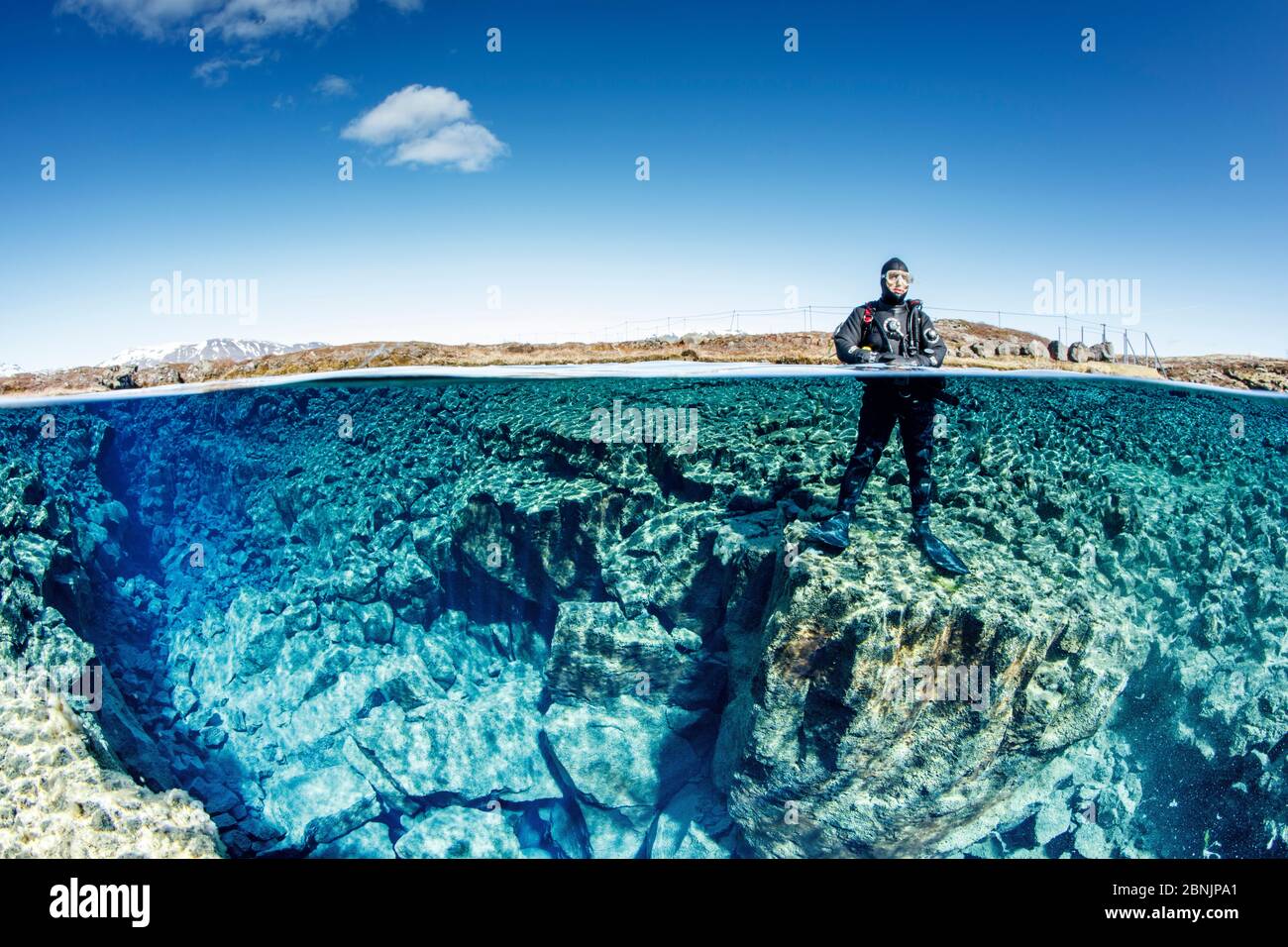 Vue sur deux niveaux de l'homme posant sur le bord de la petite fissure, situé sur le côté gauche de Silfra Lagoon, parc national de Thingvellir, Islande. Banque D'Images