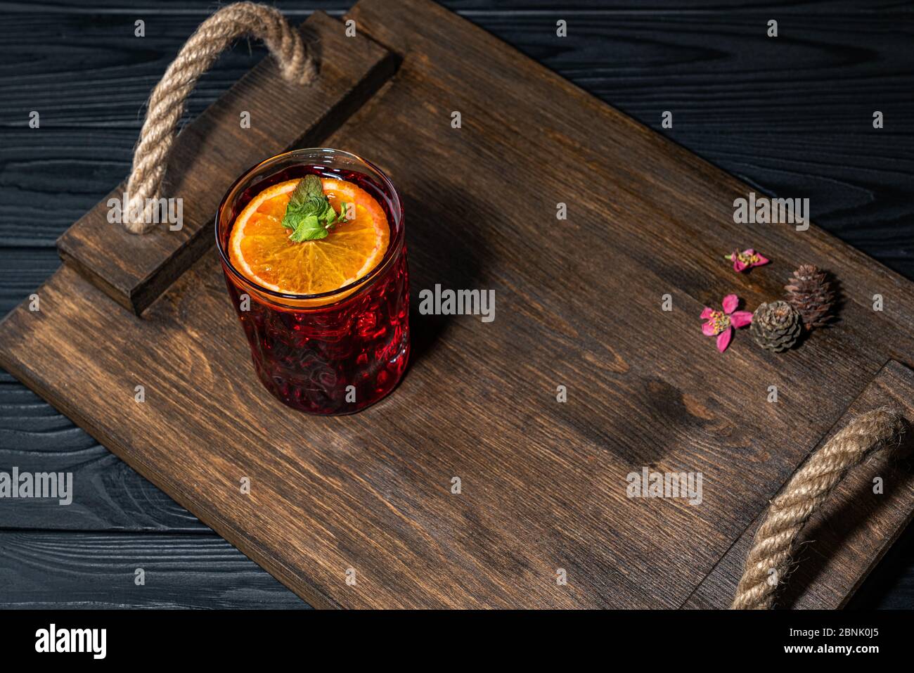 Cocktail traditionnel rouge vif avec whisky sur une planche en bois. Décoration avec des cônes et des petites fleurs roses. Exemple de service parfait Banque D'Images