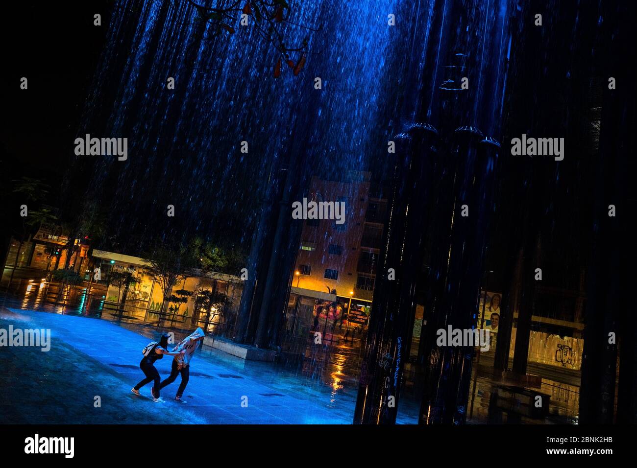 Un jeune couple colombien, se poursuivant, joue autour dans la cascade de rideau de pluie dans le parc Las Chimeneas à Itagüí, Colombie. Banque D'Images