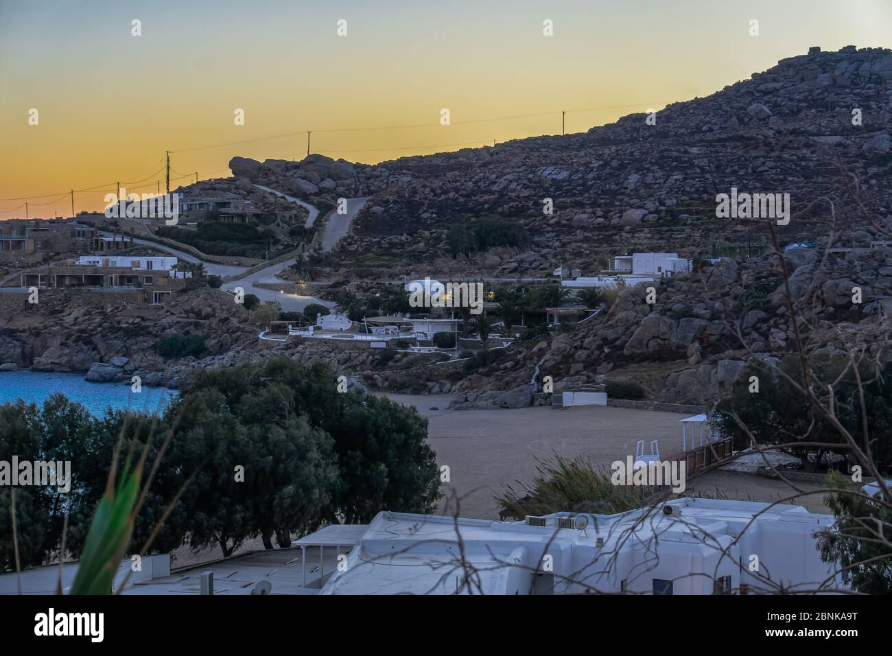 Plage de sable vide de côte sous la colline rocheuse à l'heure d'or. Vue en soirée sur la plage de Mykonos Greece Super Paradise Beach avec des bâtiments aux Cyclades. Banque D'Images