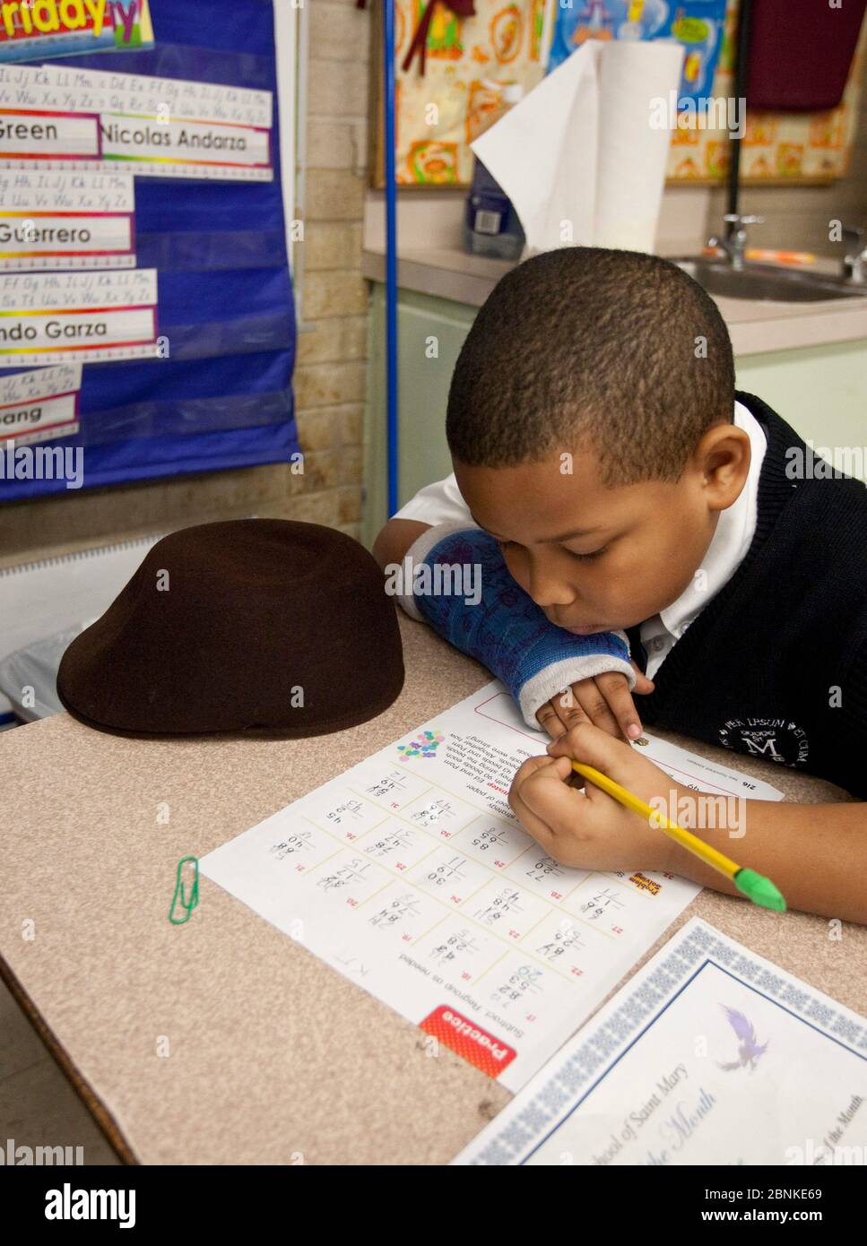 Austin Texas USA, janvier 2013: Le garçon noir de deuxième classe portant l'uniforme utilise un crayon avec la gomme verte à l'extrémité pour compléter une feuille de travail dans sa classe dans une école privée catholique. ©Bob Daemmrich Banque D'Images