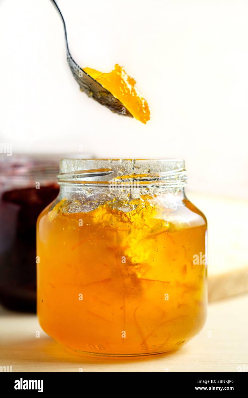 marmelade d'orange maison cueillant la confiture dans un pot en verre petit déjeuner sucré sur fond de bois clair Banque D'Images