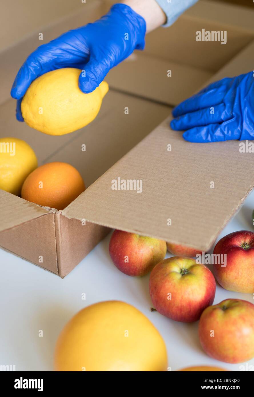 Portez des gants médicaux de protection en mettant les fruits dans la boîte de dons. Banque D'Images