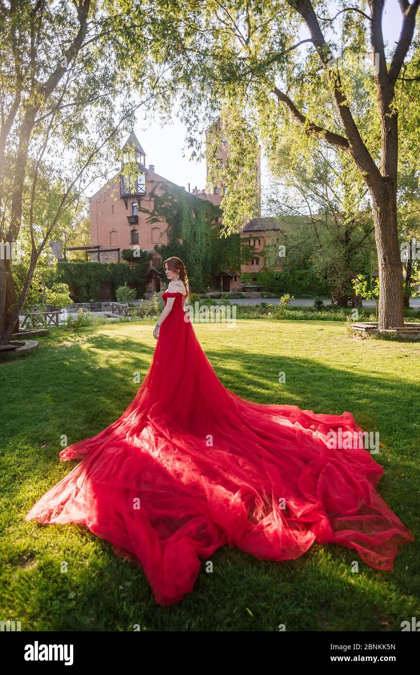 Belle femme à tête rouge tatembout en robe rouge longue posant près du château Banque D'Images
