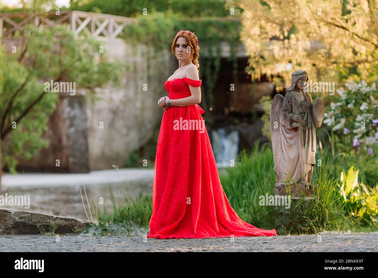 Belle femme à tête rouge tatembout en robe rouge longue posant près du château Banque D'Images