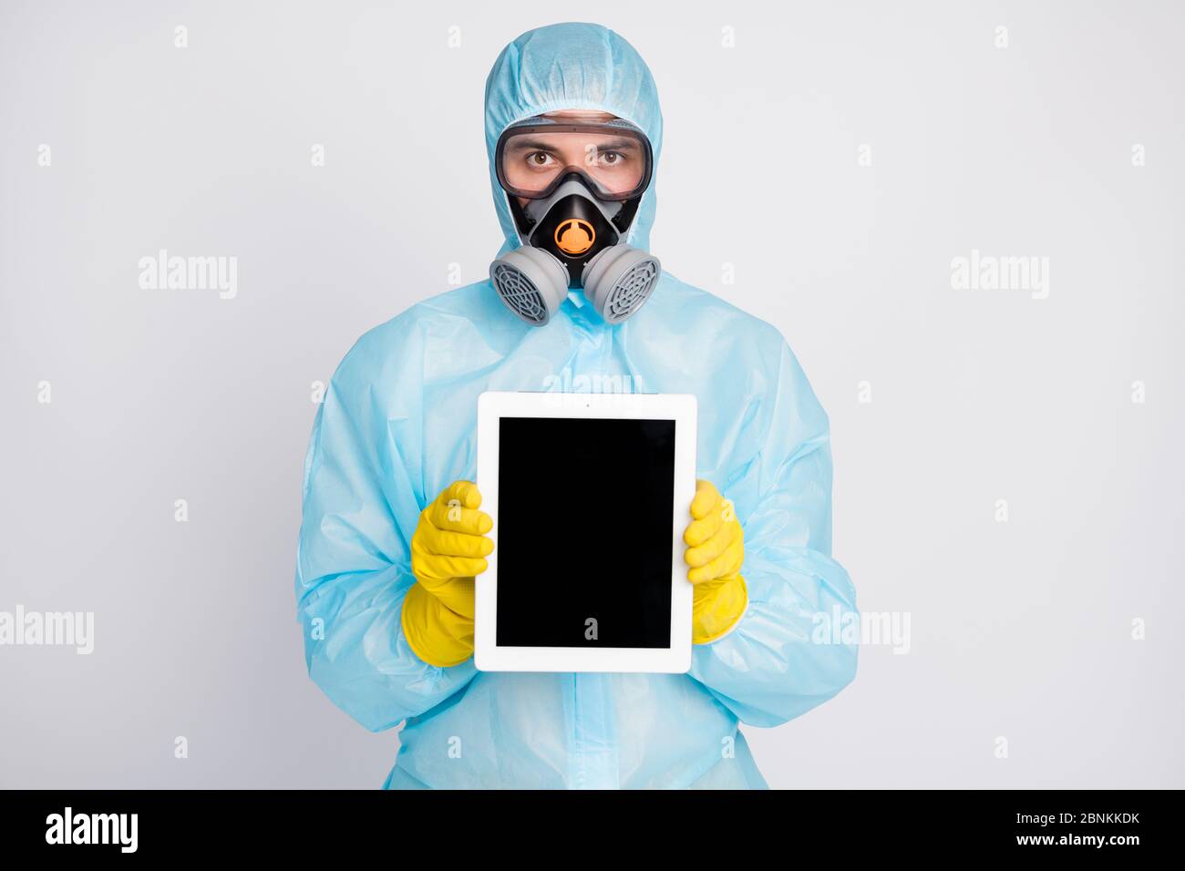 Portrait du travailleur médical homme présent comprimé porter un masque respiratoire uniforme à risque biologique isolé sur fond gris Banque D'Images