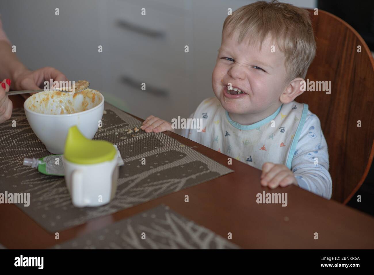 Portrait d'un bébé garçon mignon avec des cheveux dorés assis à la table ne veut pas manger porridge. Concept de style de vie. Mauvaise nourriture. L'enfant n'a pas d'appétit. Banque D'Images