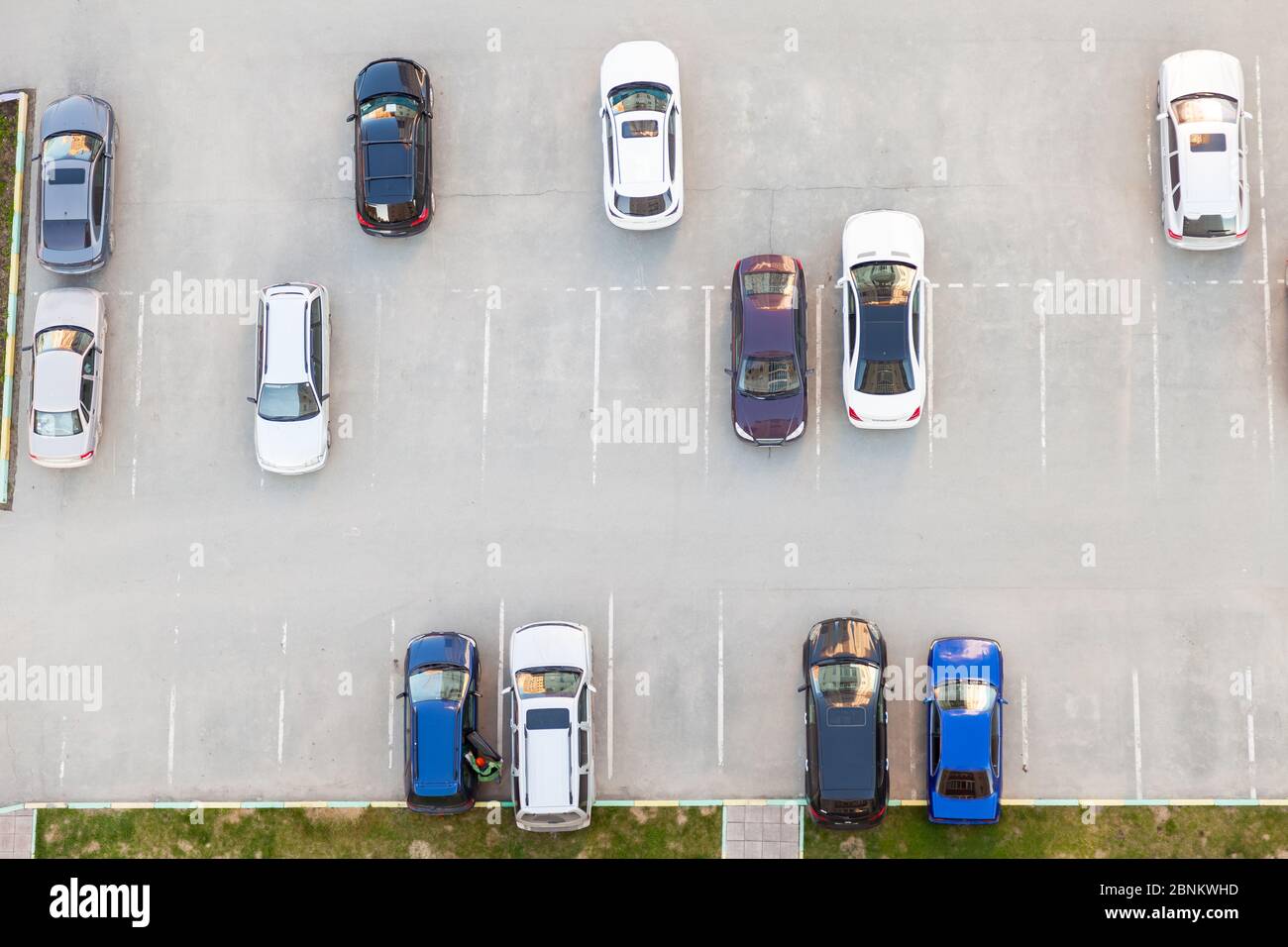 Vue de dessus d'un parking semi-vide en asphalte avec des voitures noires blanches et bleues garées près d'un immeuble résidentiel en été. Banque D'Images