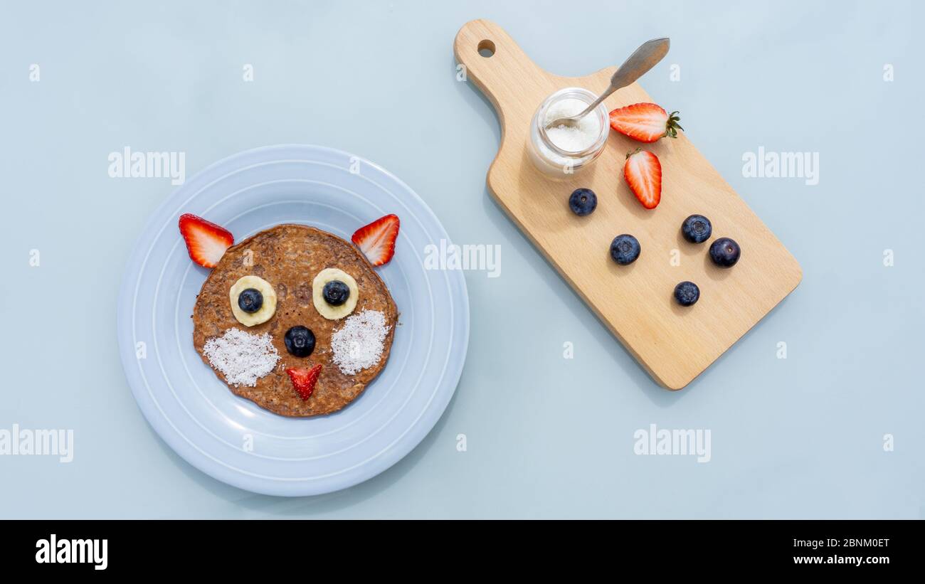 Crêpes aux flocons d'avoine créatives pour les enfants. Chat ou ours dans une plaque isolée sur fond bleu. Petit déjeuner végétarien sain, déjeuner ou en-cas. Vue de dessus, gros plan Banque D'Images
