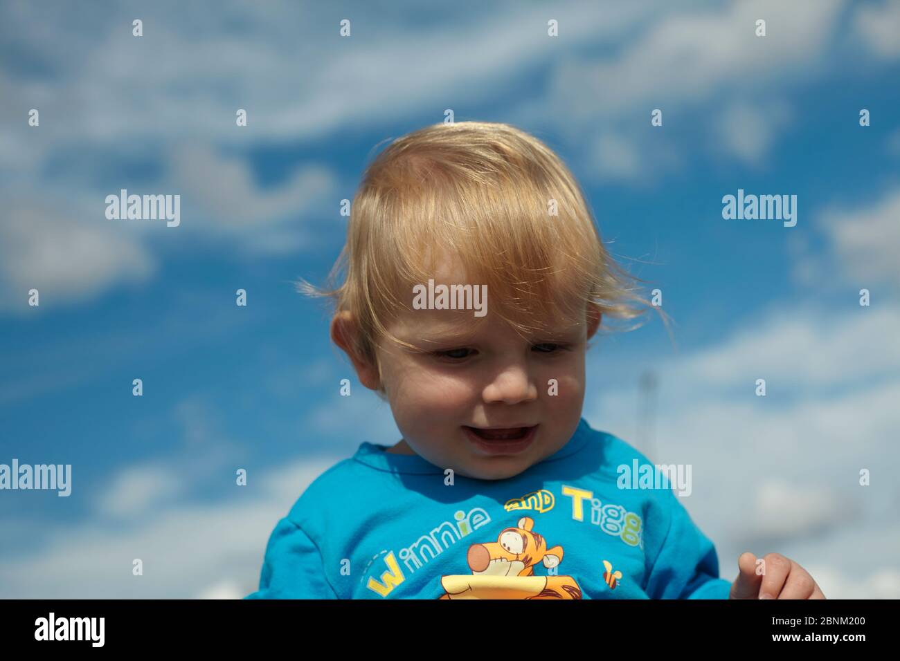 Printemps Portrait d'un bébé garçon mignon avec des cheveux dorés sur fond de ciel bleu. En plein air. Concept été et style de vie heureux. Banque D'Images