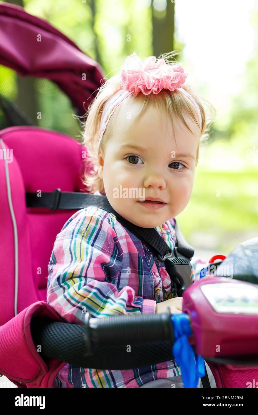 Une petite fille dans un arc sur sa tête s'assoit au volant d'un vélo. Les premiers enfants à vélo. Promenade d'été avec bébé Banque D'Images