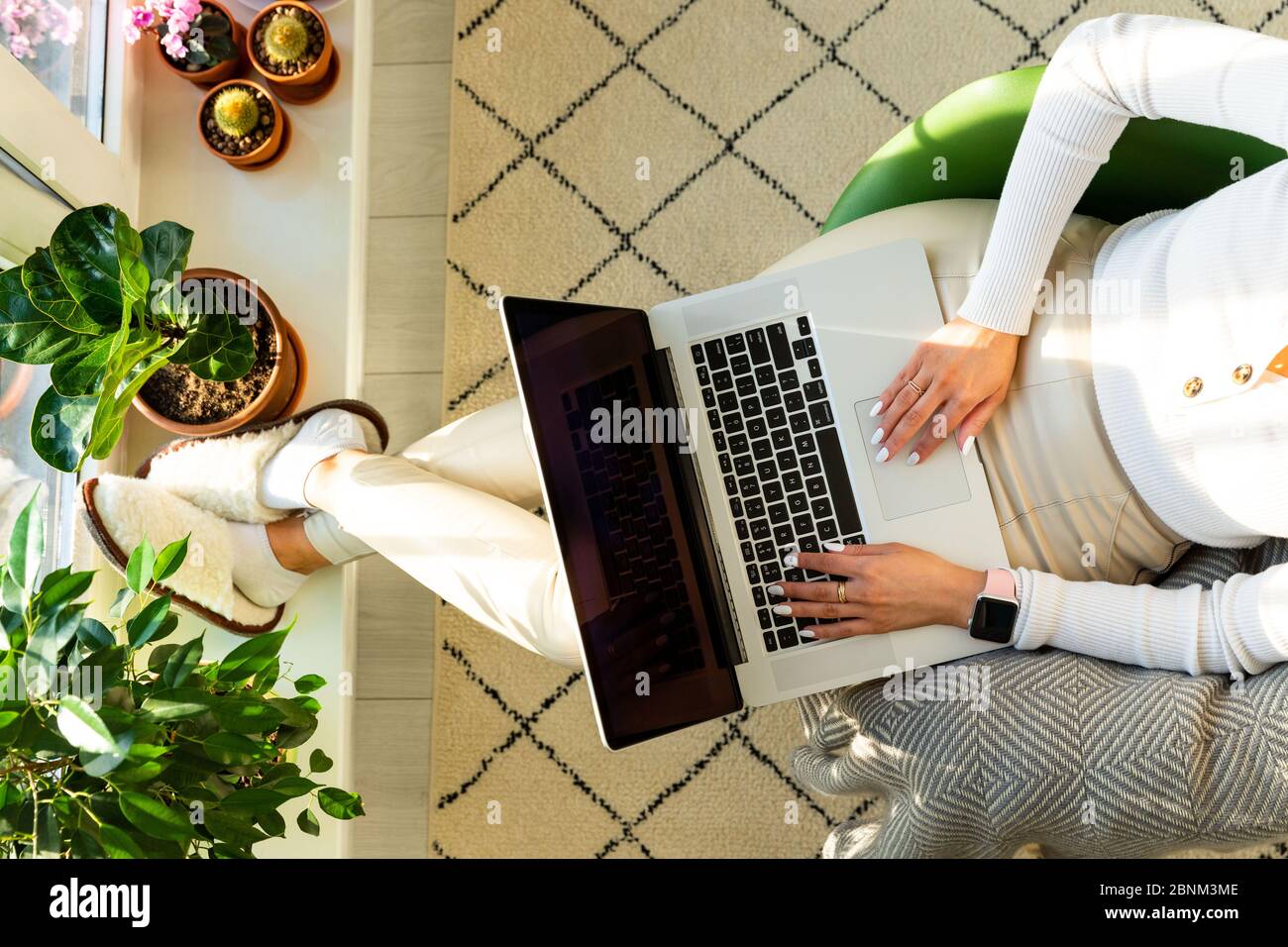 Femme assise sur un fauteuil et mettant vos pieds sur le rebord de la fenêtre avec des plantes de maison dans la cuve, travaille sur ordinateur portable à la maison pendant l'auto-isolation. Bus Banque D'Images