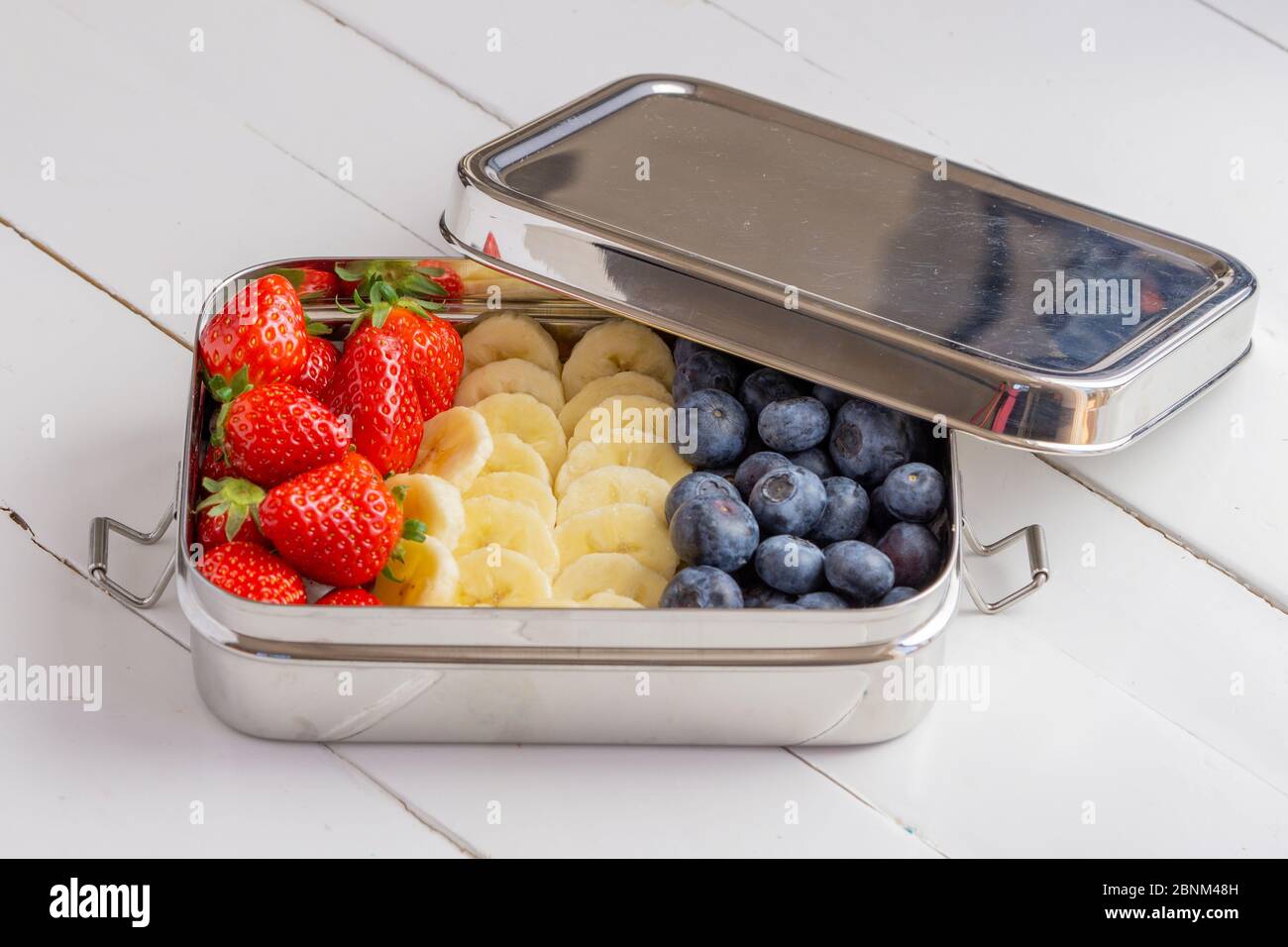 En-cas bleuets, bananes et fraises dans un grand récipient en acier inoxydable. Boîte à lunch sans plastique isolée sur fond blanc. Zéro déchet, écologique. Banque D'Images