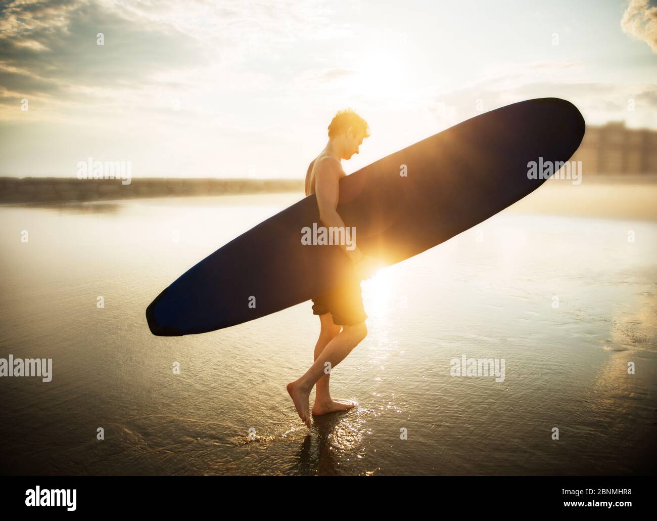 Jeune homme marchant sur la plage avec un surf Banque D'Images