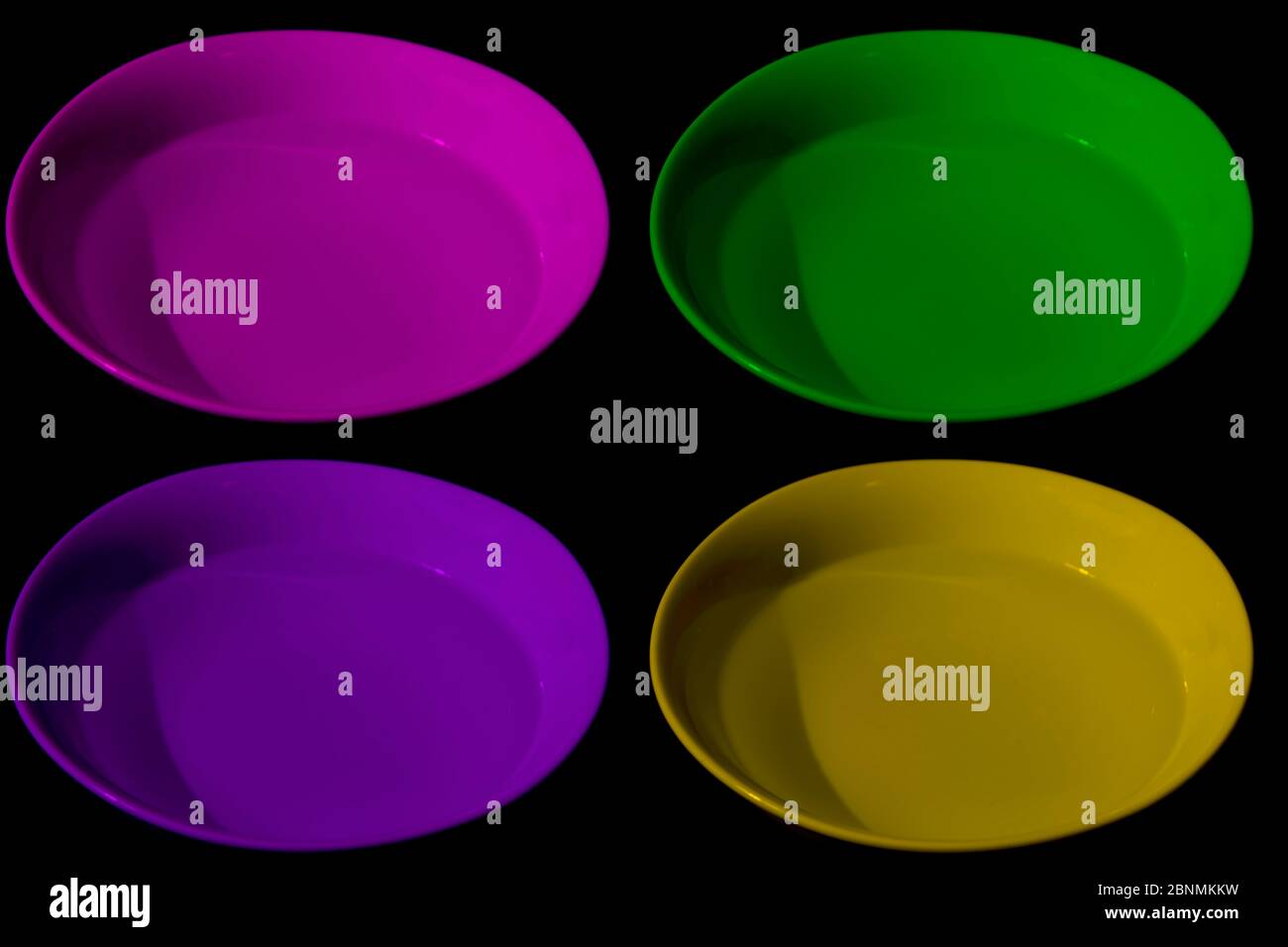 Quatre bols avec eau de différentes couleurs, magenta, jaune, violet et vert, fond noir, couleurs complémentaires Banque D'Images
