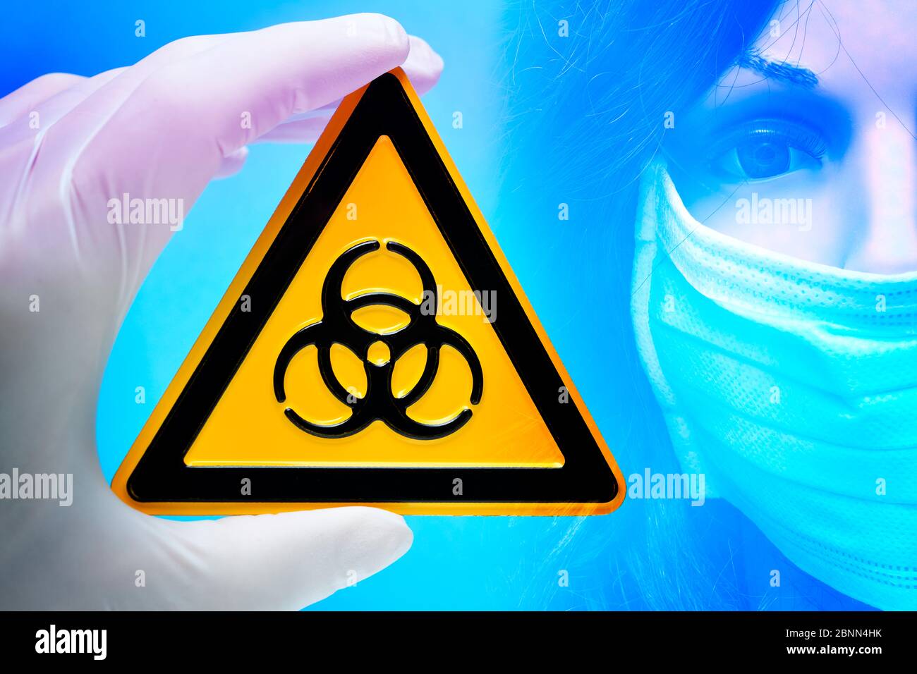 Photo montage, signe de danger biologique est tenu par une main devant une femme avec un masque facial, photo symbolique virus corona Banque D'Images