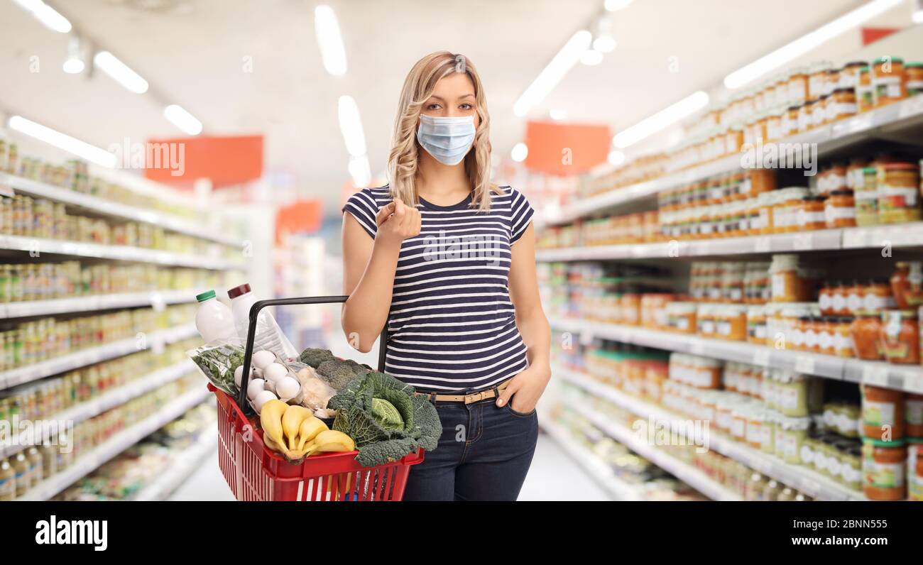 Jeune femme portant un masque facial de protection et portant un panier dans un supermarché Banque D'Images