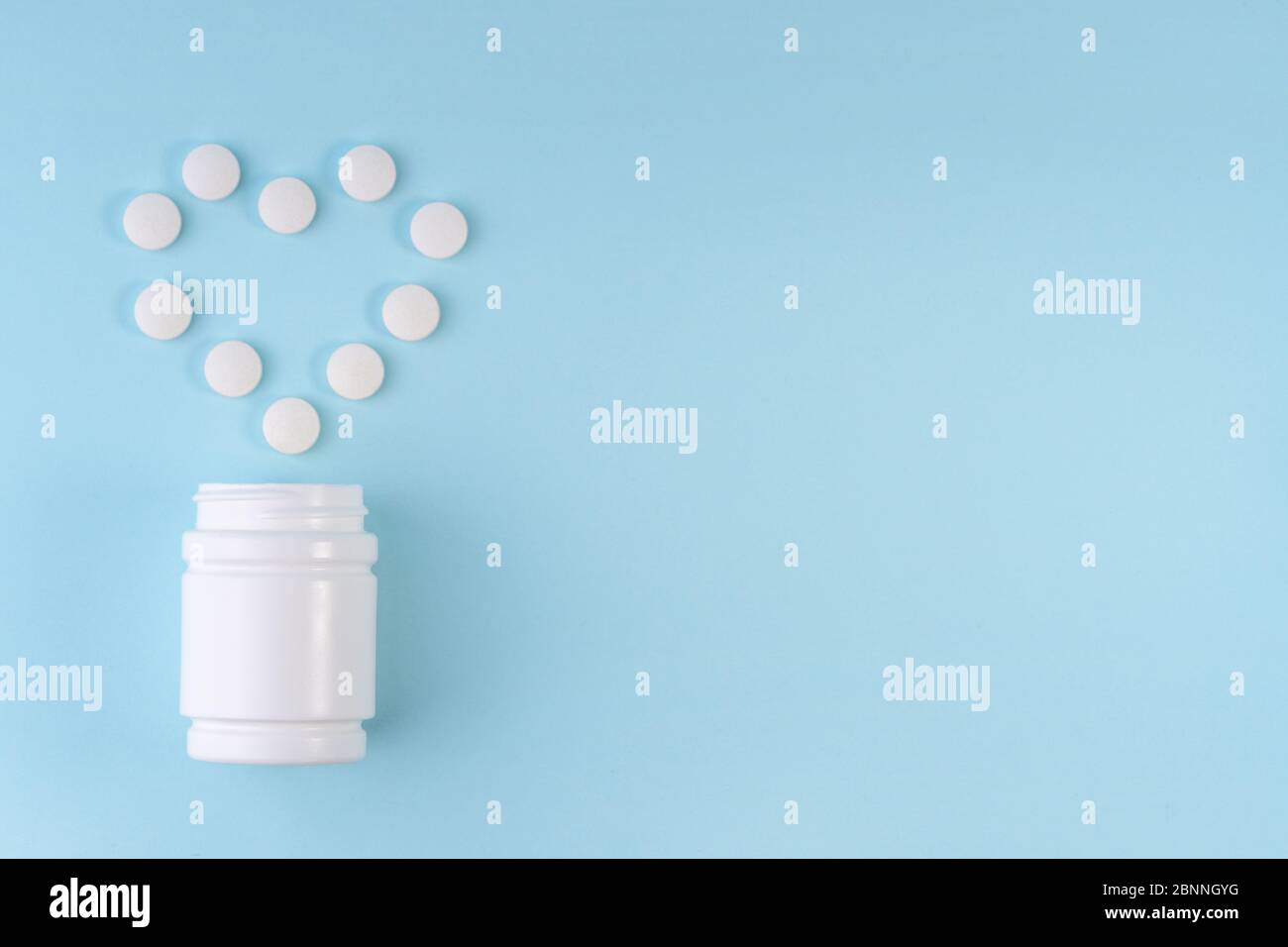 Les pilules blanches de médecine se répande de bouteille dans le coeur forme sur bleu. Comprimés de maladies cardiaques. Symbole médicament et cœur. Santé, assurance santé Banque D'Images