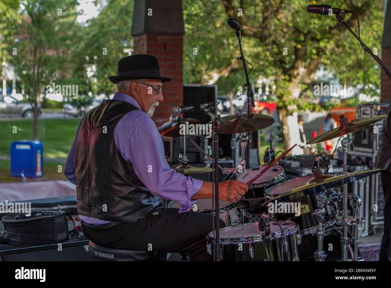 Homme âgé, habillé en coup sec, avec chapeau fedora, jouant à la batterie, dans le groupe rock au concert d'outoor. Banque D'Images