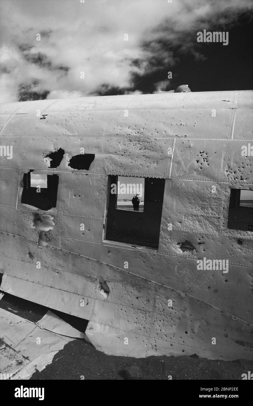 Homme dans une fenêtre d'une épave d'avion DC3 abandonnée sur la plage noire à Sólheimasandur contre ciel sombre Banque D'Images