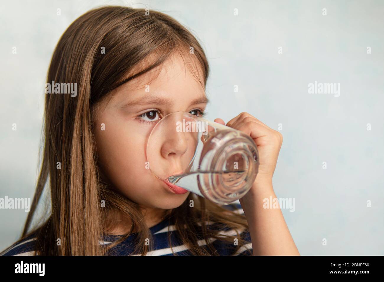 Une petite fille boit de l'eau dans une tasse de verre. Une petite fille tient un verre d'eau. Soif d'eau Banque D'Images
