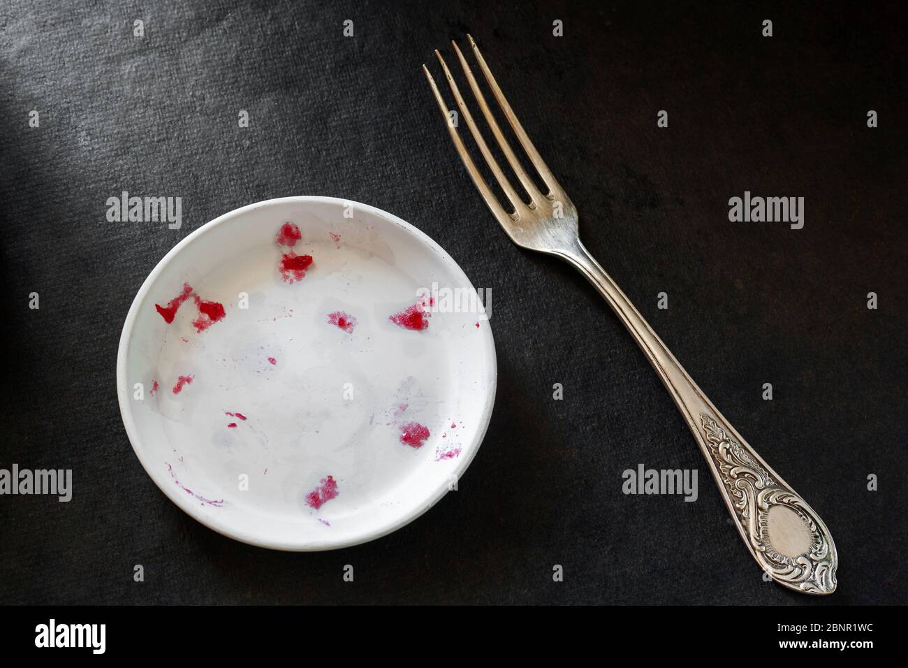 Un dessert très savoureux est terminé. Assiette blanche vide avec les restes d'un dessert sucré et une fourchette sur fond sombre. Banque D'Images