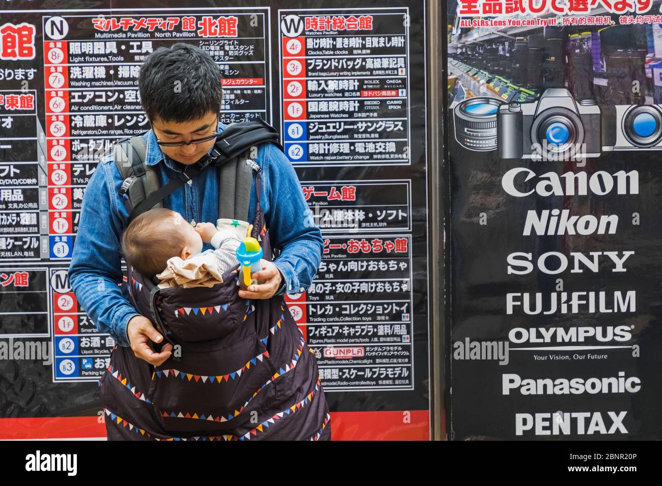 Japon, Honshu, Tokyo, Père Nourrir Bébé Devant La Boutique De Caméras Banque D'Images