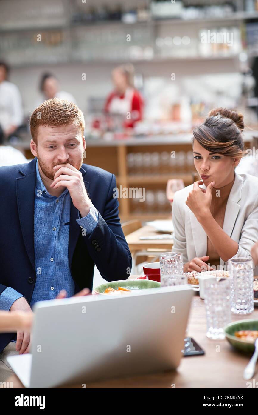 jeune homme et femme caucasien adulte regardant du contenu sur ordinateur portable pensant, en considérant l'idée d'affaires, dans le restaurant à l'heure du déjeuner Banque D'Images