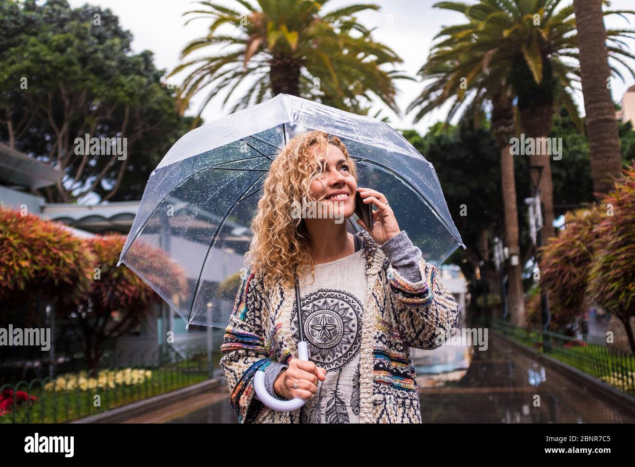 Belle et gaie tendance jeune femme caucasienne de mode à la mode dans la ville sous la pluie avec un parapluie transparent - saison froide concept appréciant le parc urbain Banque D'Images