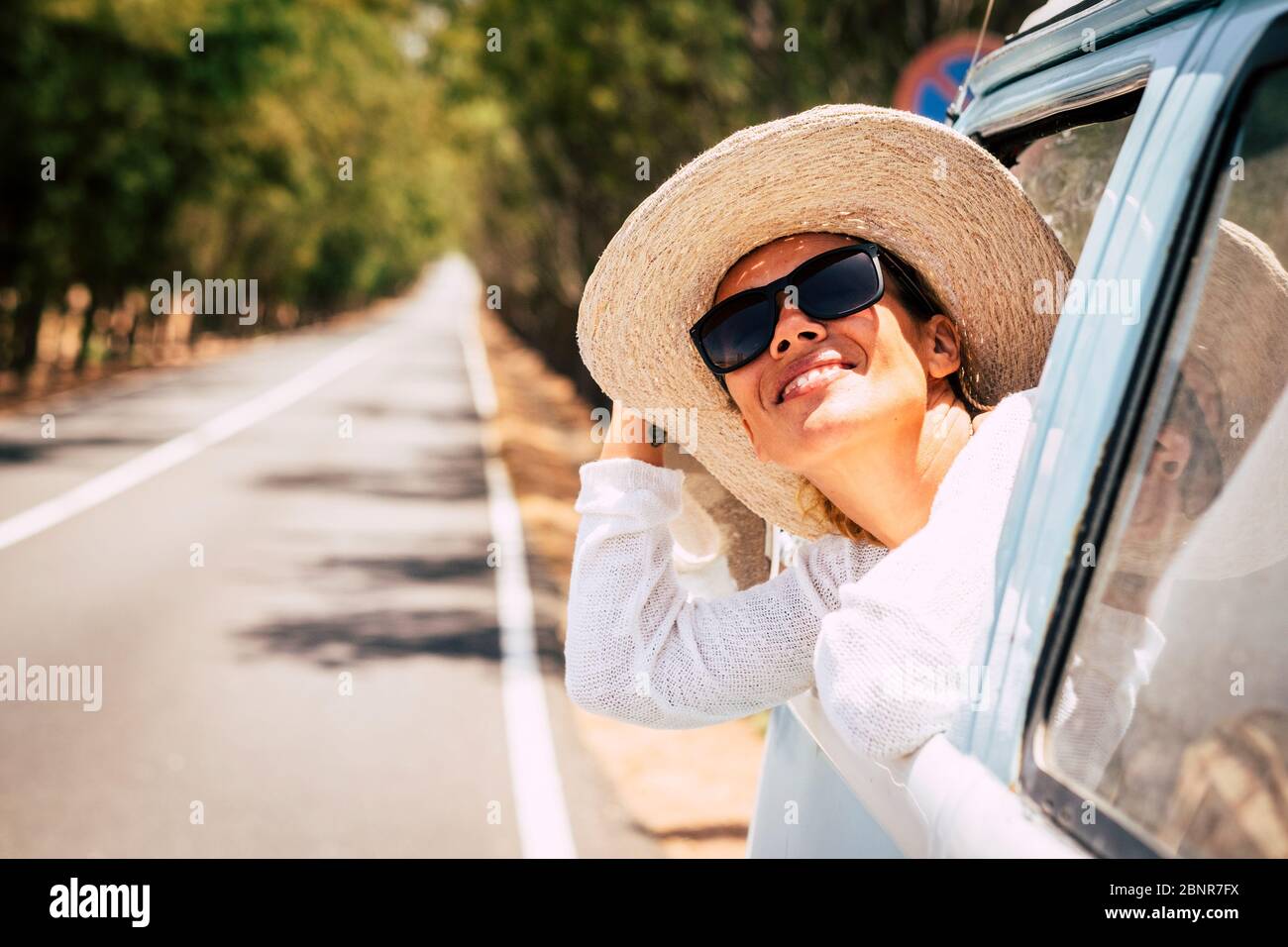 Heureux jeunes belles caucasiens les femmes aiment le soleil à l'extérieur de la fenêtre de vieux véhicule bleu - longue route en arrière-plan pour le voyage et le concept de transport avec le bonheur et le mode de vie joyeux Banque D'Images