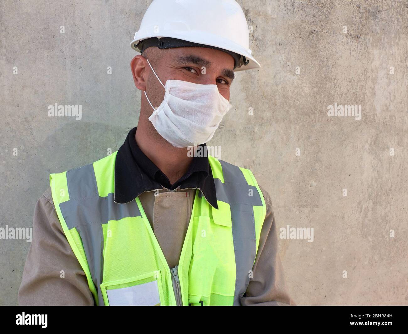 L'ingénieur civil porte un masque médical de protection contre un mur en béton sur le chantier de construction. Banque D'Images