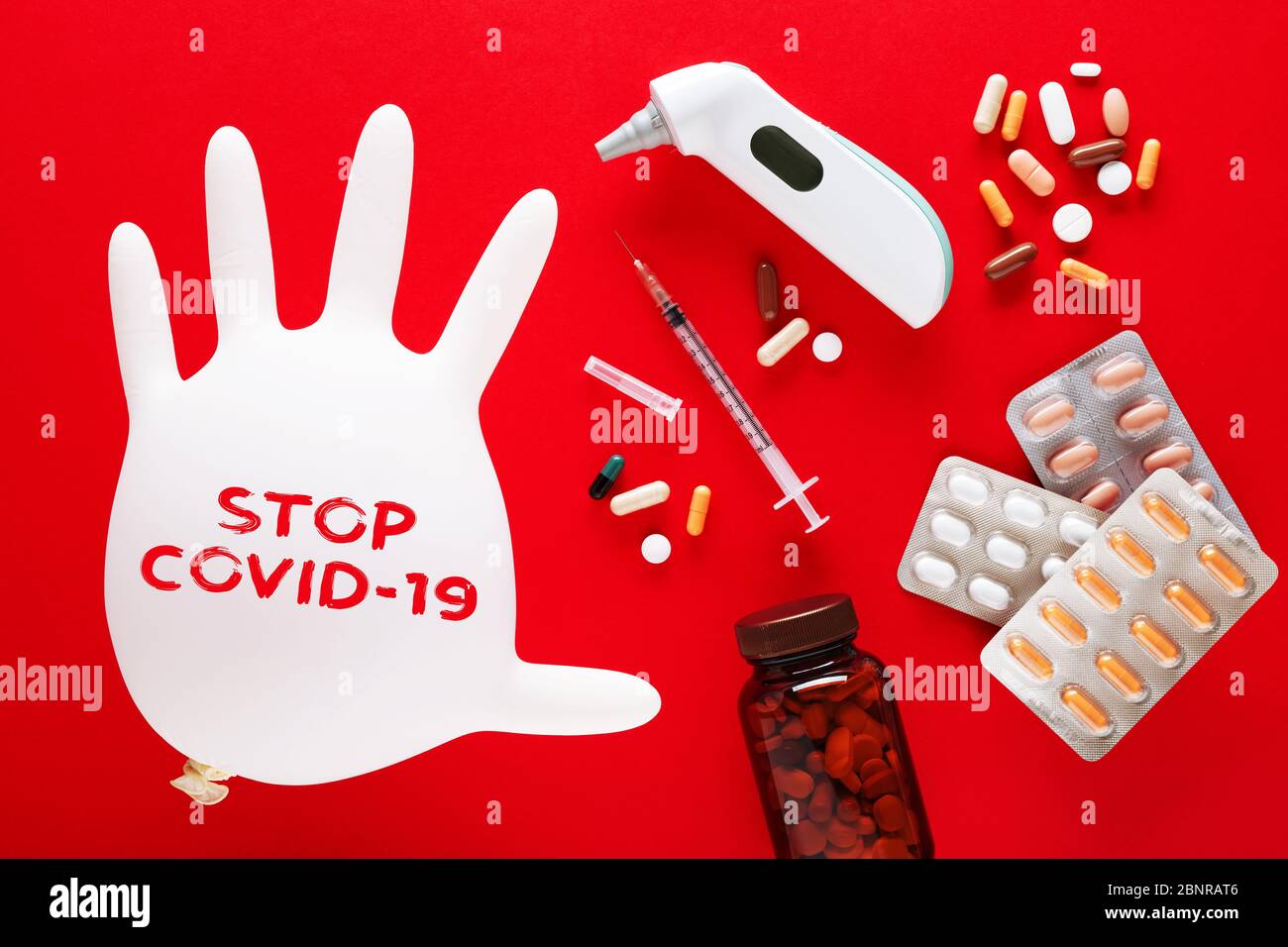 Gant médical gonflé avec message texte STOP Covid-19, seringue, pilules et thermomètre sur fond rouge. Traitement du virus Corona ou de la maladie covid 19 o Banque D'Images