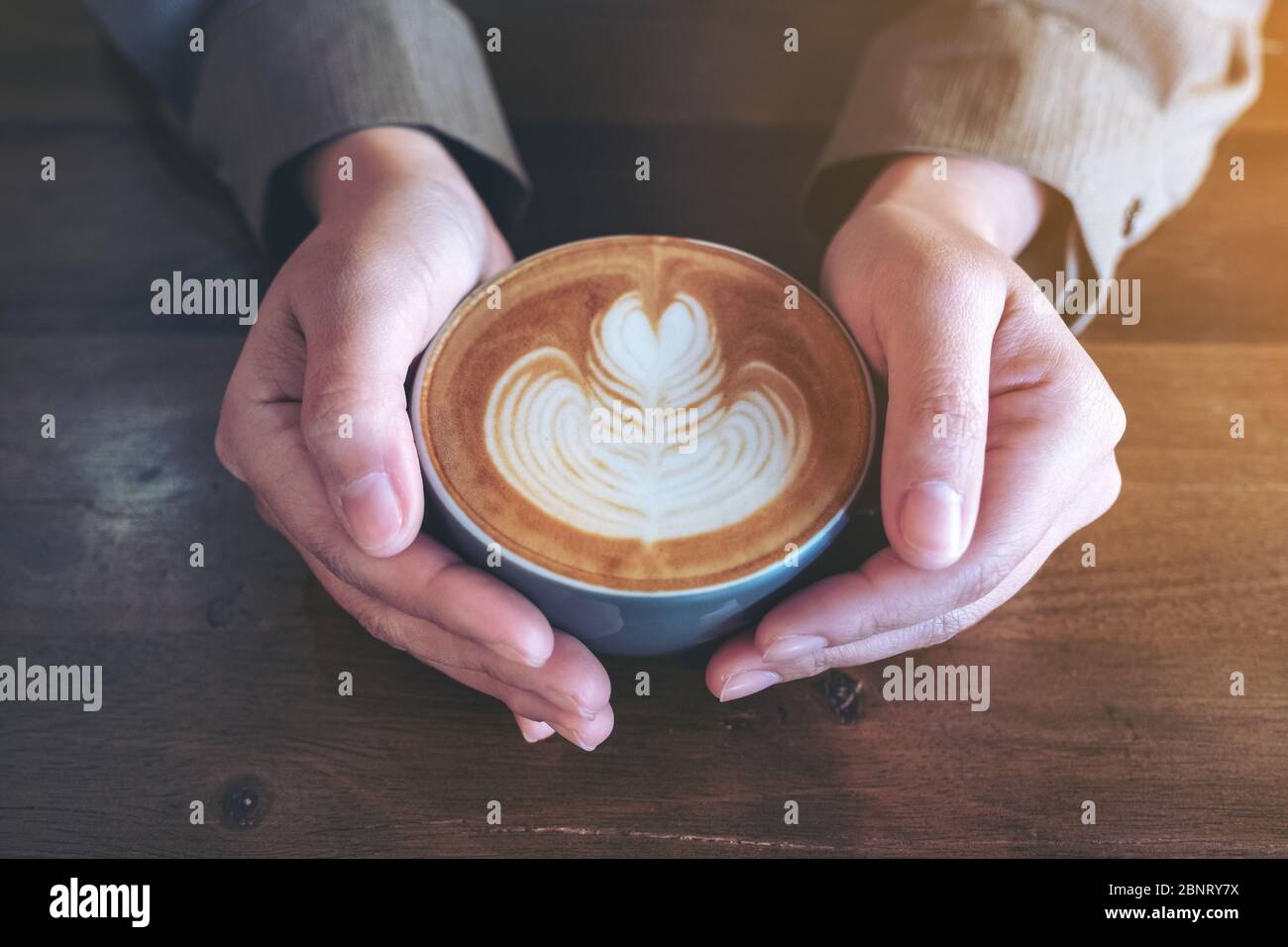 Gros plan de mains tenant une tasse bleue de café latte chaud avec art latte sur une table en bois dans le café Banque D'Images