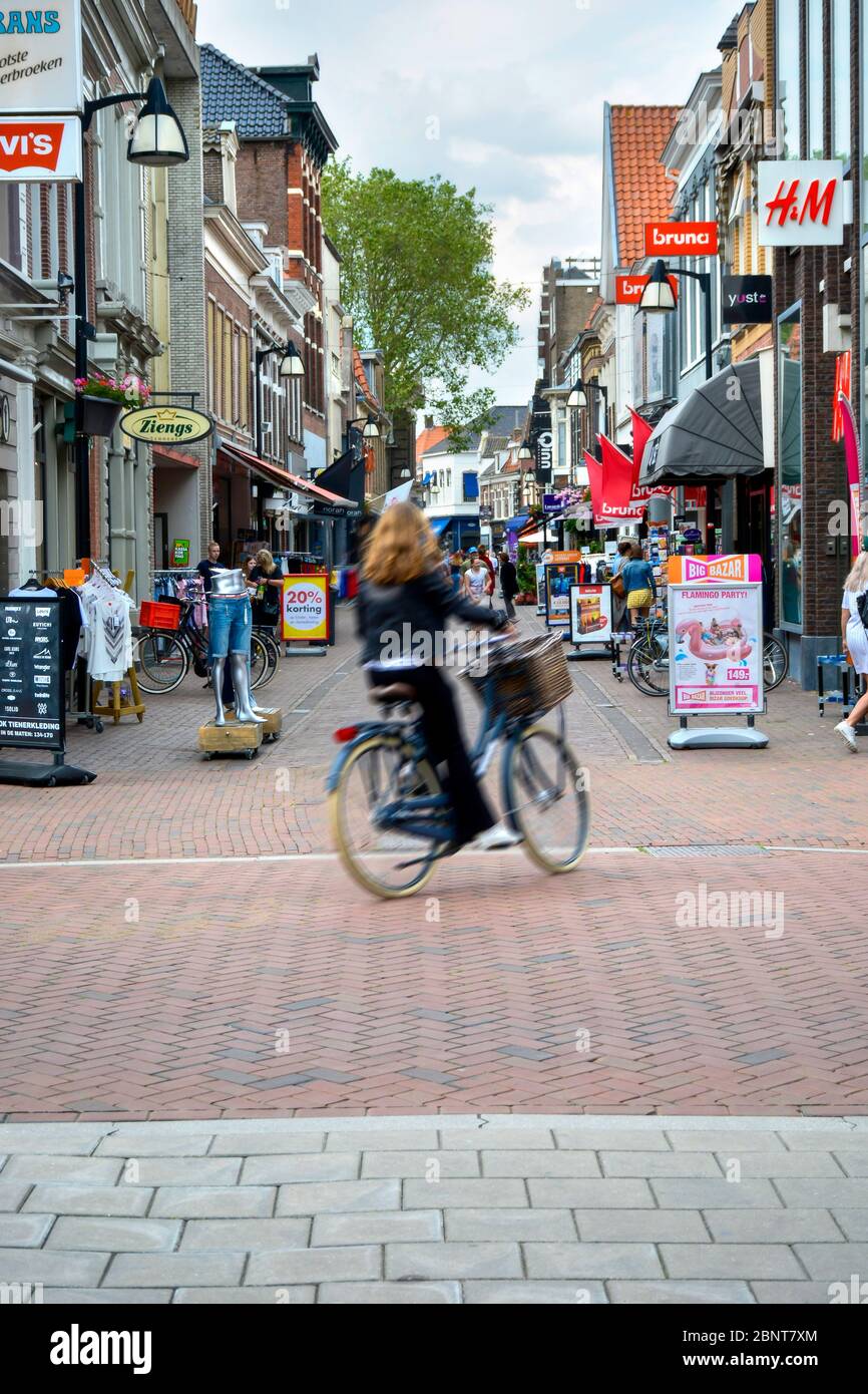 Rue commerçante dans le centre de Meppel. Les gens magasinent en arrière-plan. Une fille passe à vélo. Flou de mouvement. Banque D'Images