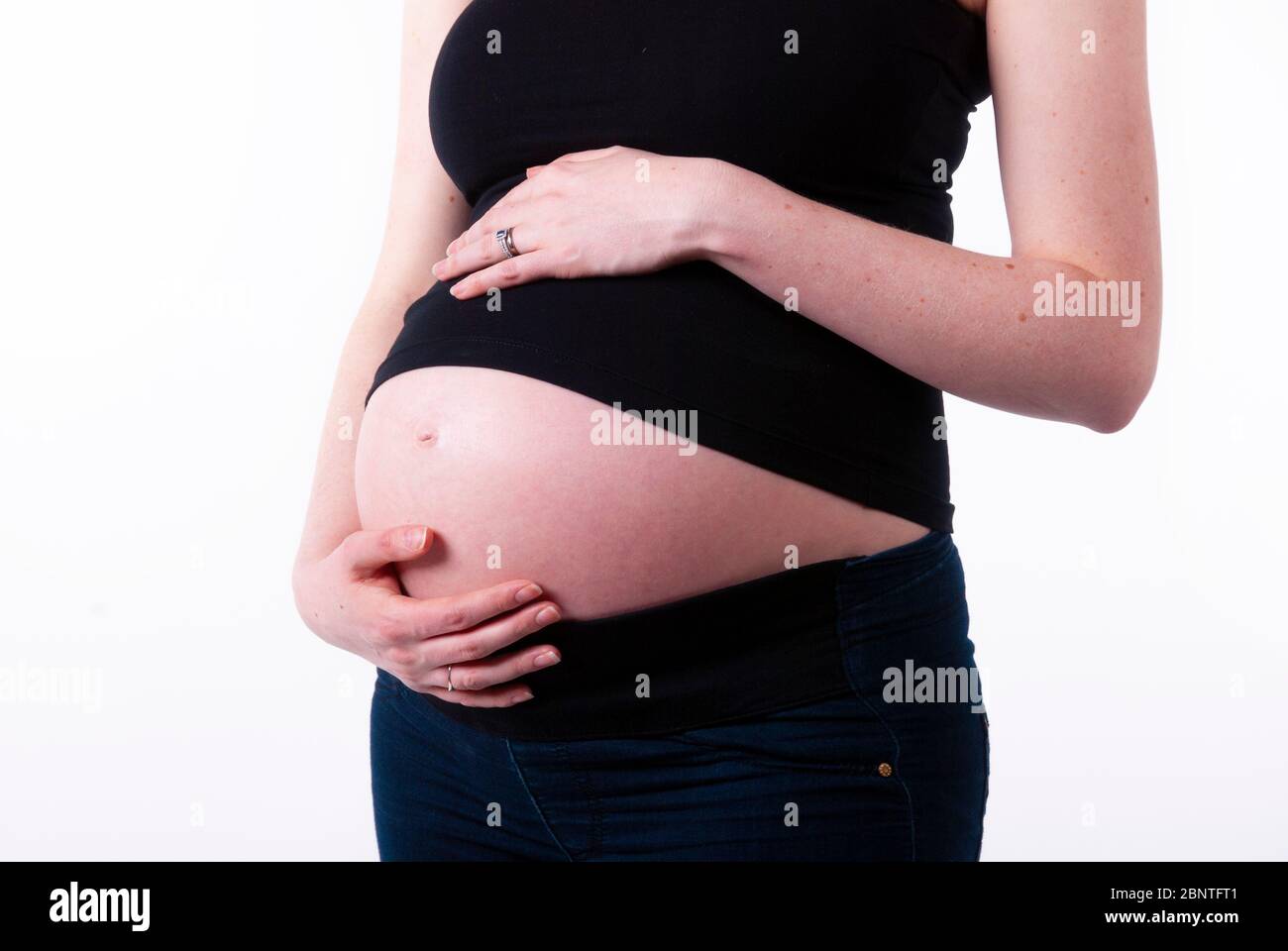 Photo studio d'une jeune femme enceinte vêtue de vêtements décontractés noirs tenant son ventre exposé. Banque D'Images