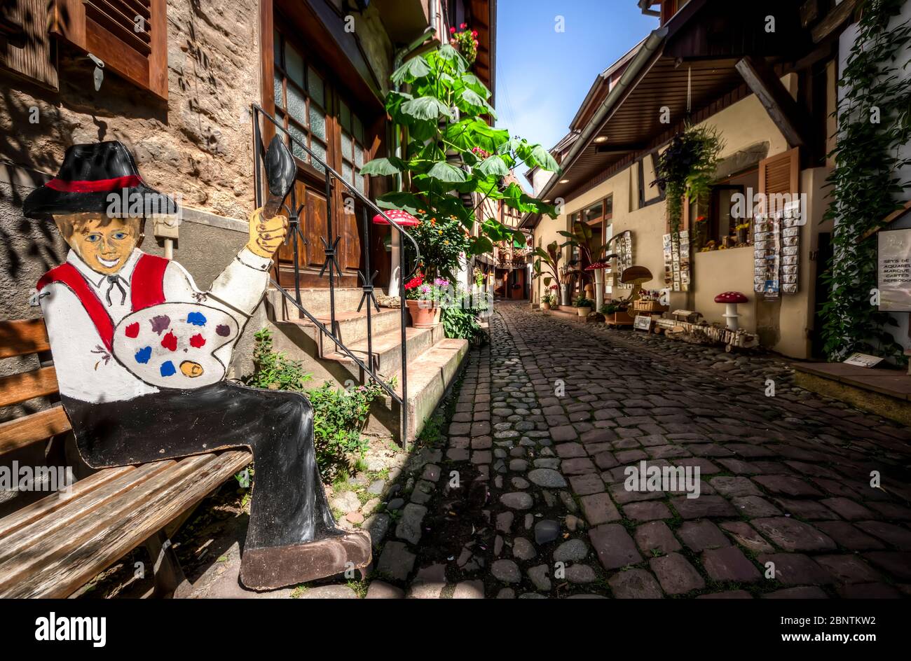 Rue pavée touristique de la vieille ville d'Eguisheim avec des boutiques et un mannequin en bois artisanal d'un peintre Banque D'Images