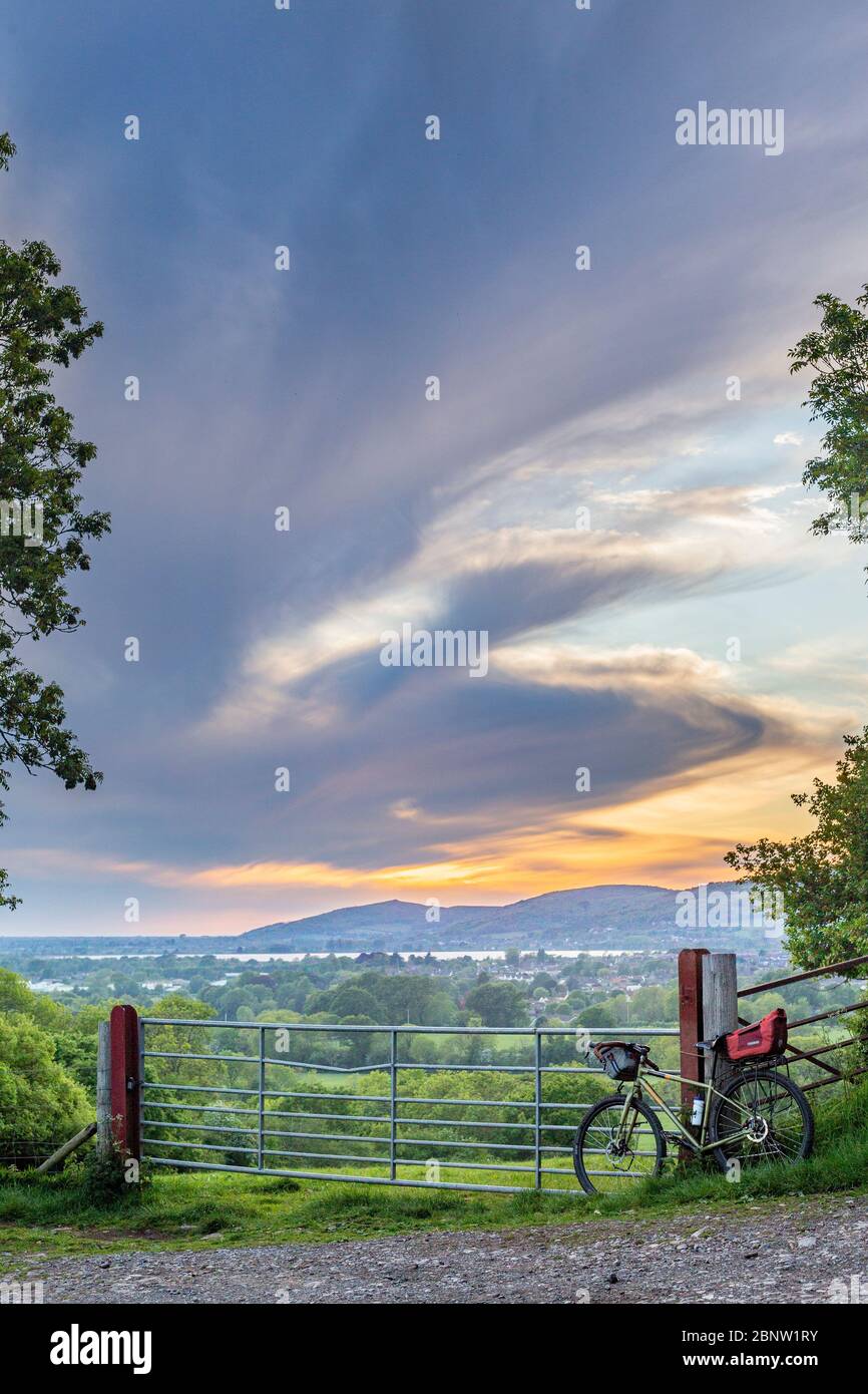 Un vélo se penche contre une porte donnant sur le réservoir de cheddar avec les collines de mendip et les nuages spectaculaires formant le fond (format portrait) Banque D'Images
