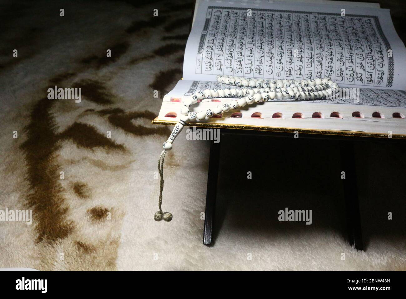 Livre du Coran sur un tapis marron, ouvert et isolé sur fond sombre Banque D'Images