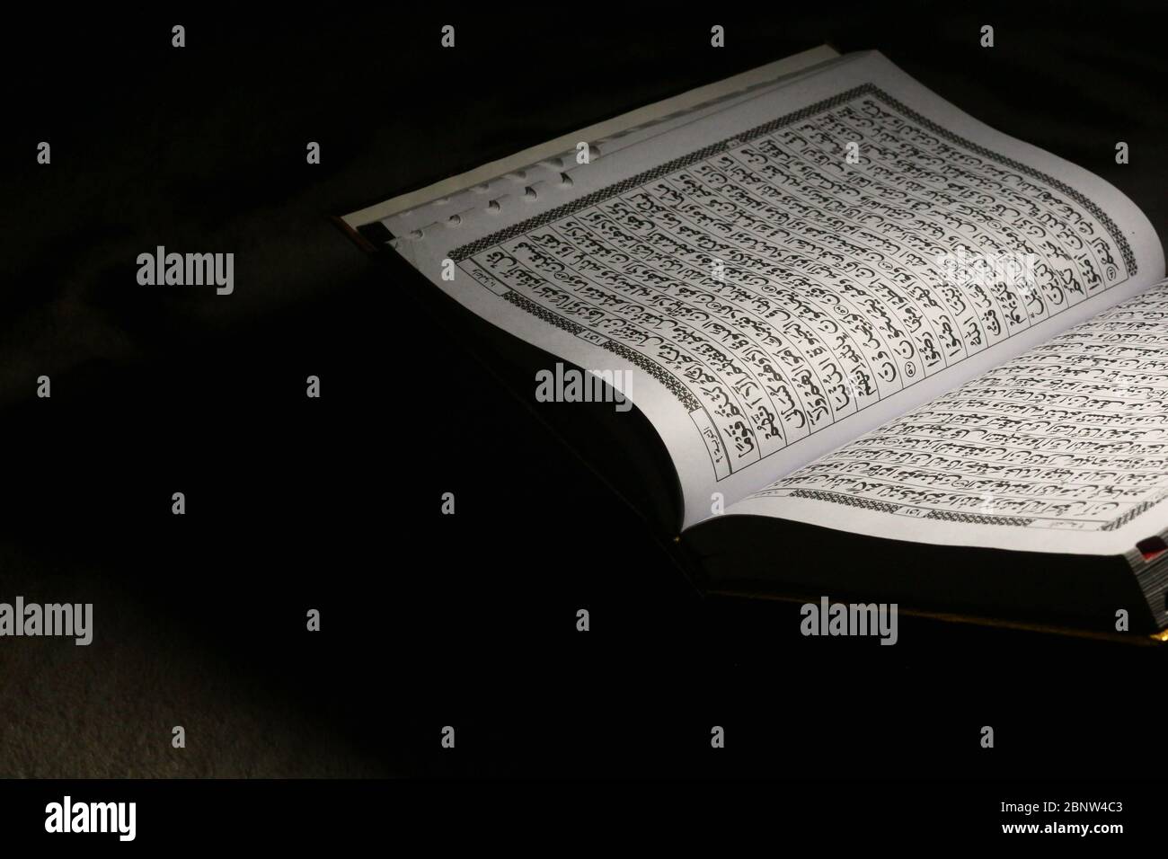 Livre du Coran sur un tapis marron, ouvert et isolé sur fond sombre Banque D'Images